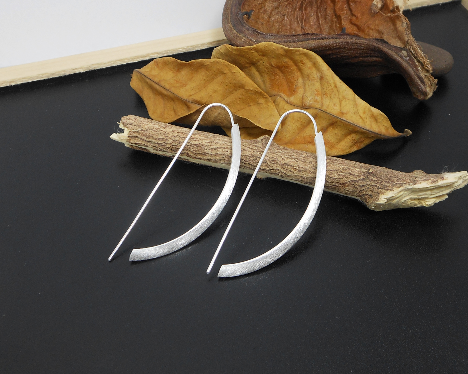 Silver arc D-hoop threader earrings resting on a wooden surface.