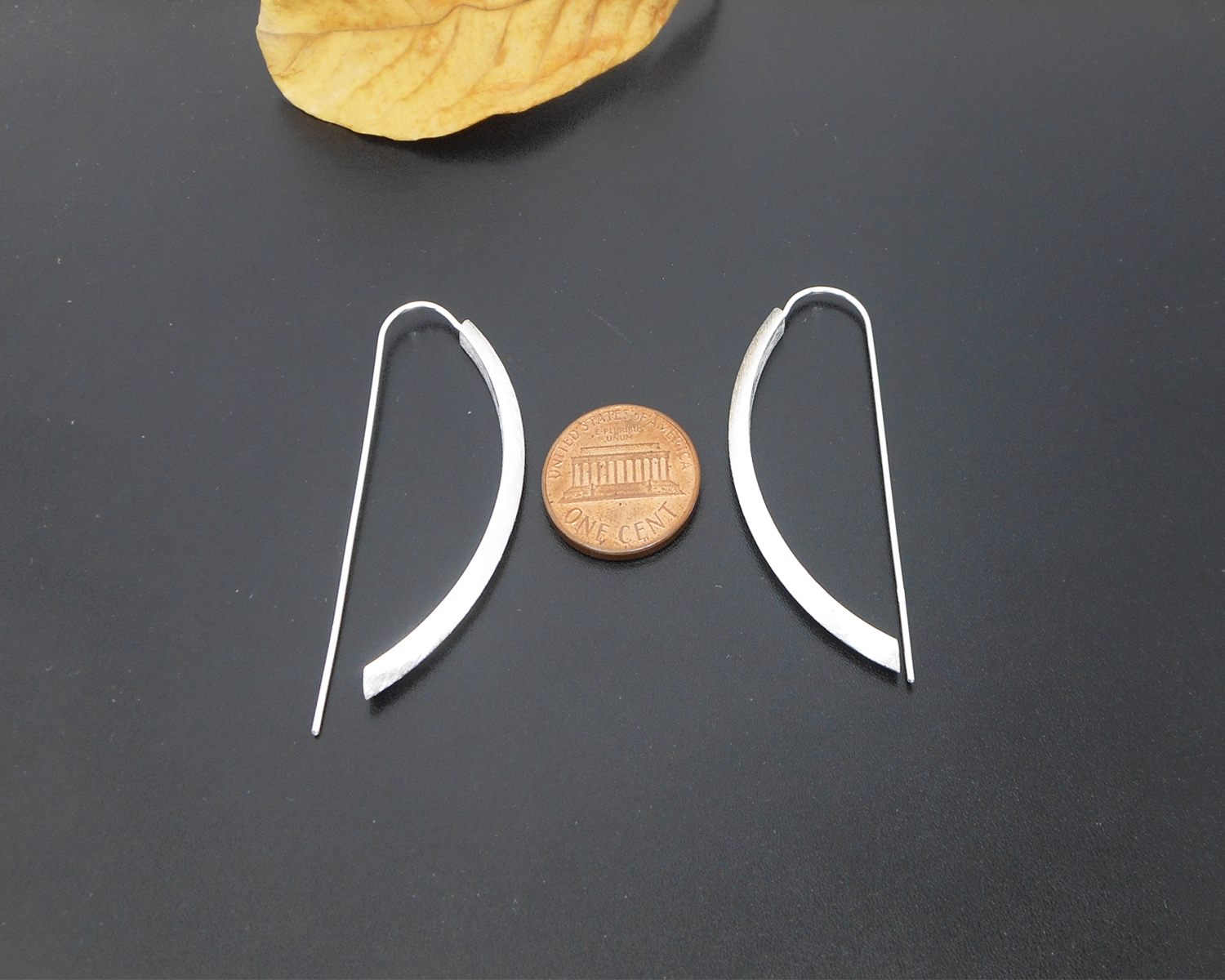 Silver arc D-hoop threader earrings displayed next to a coin for scale.