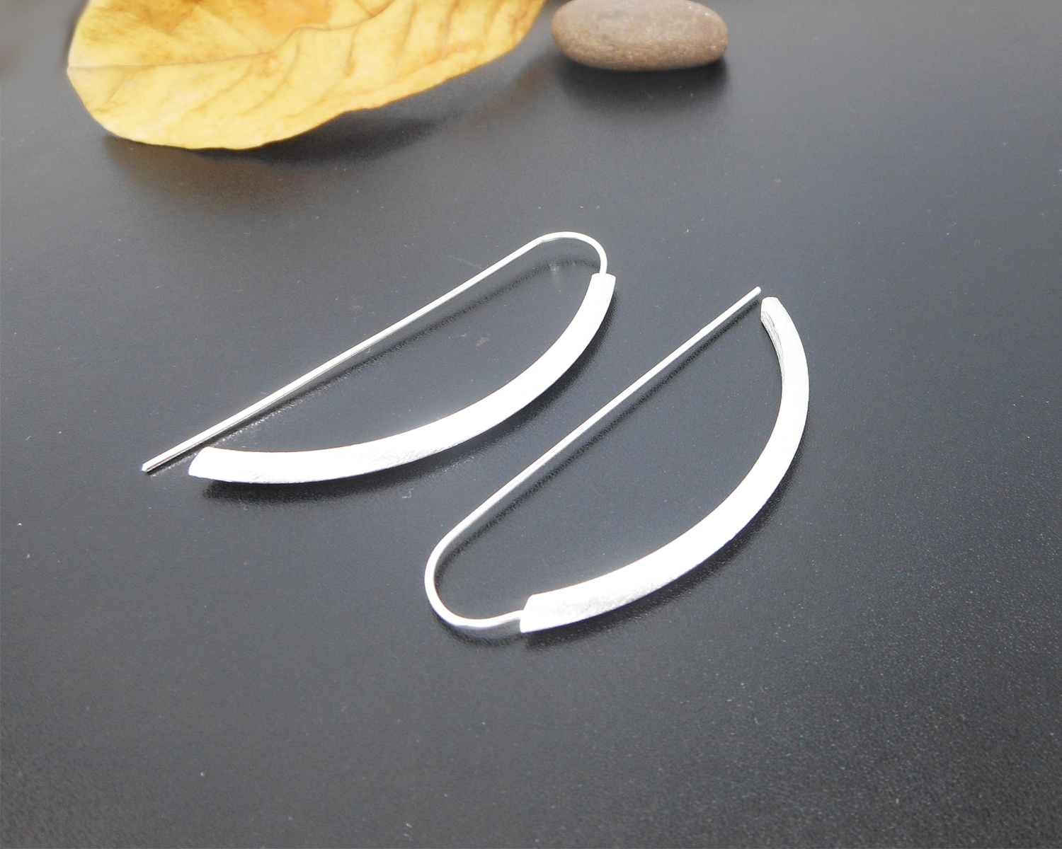 Angle view of sterling silver arc D-hoop threader earrings.