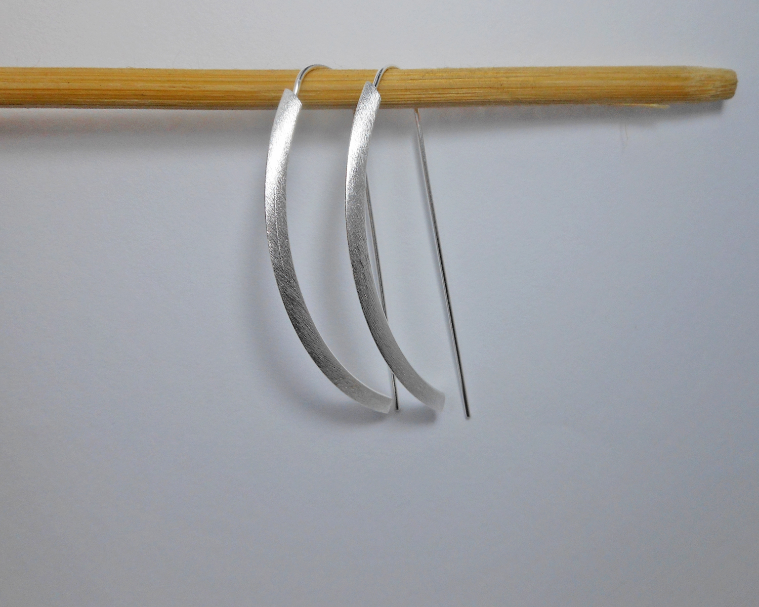 Silver arc D-hoop threader earrings hanging from a wooden prop.