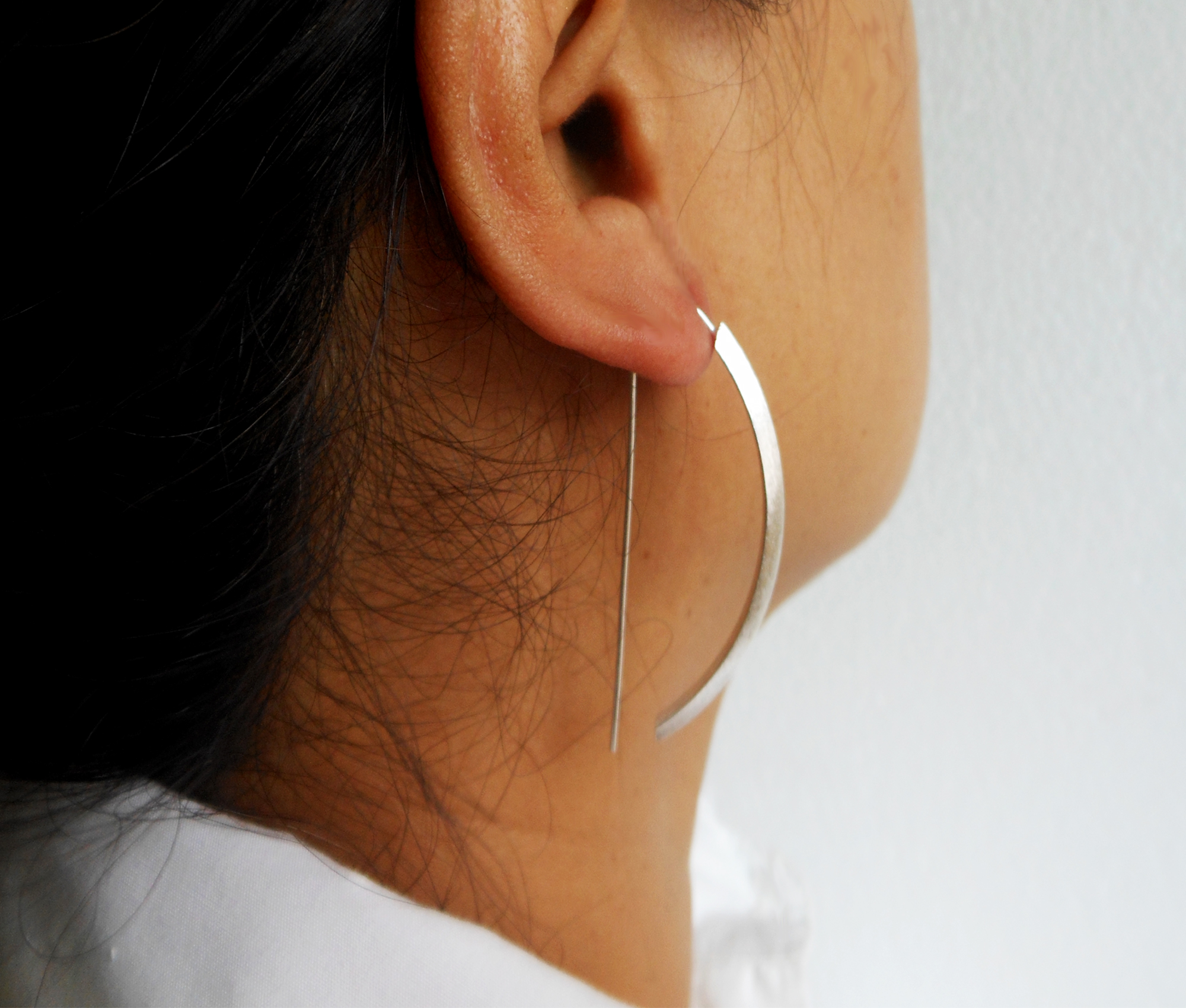 Close-up side profile of a model wearing silver arc D-hoop threader earrings.