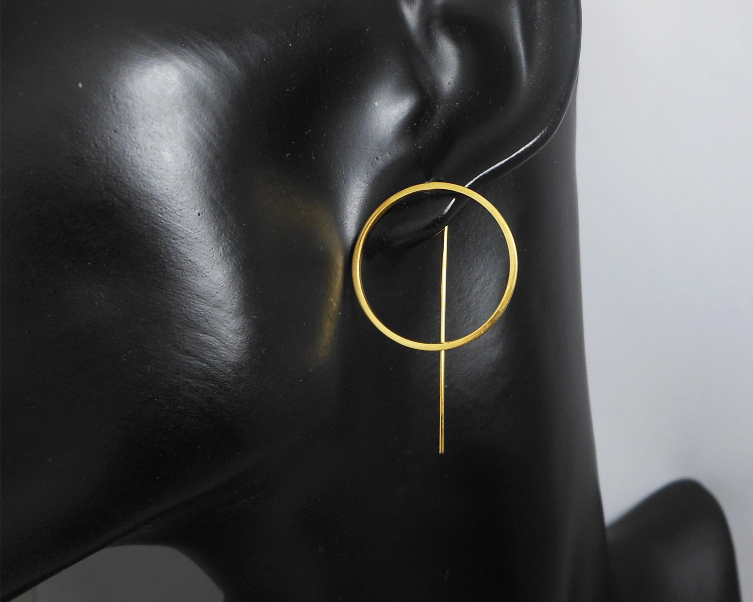 Close-up view of gold-plated circle threader earrings on a black mannequin bust.