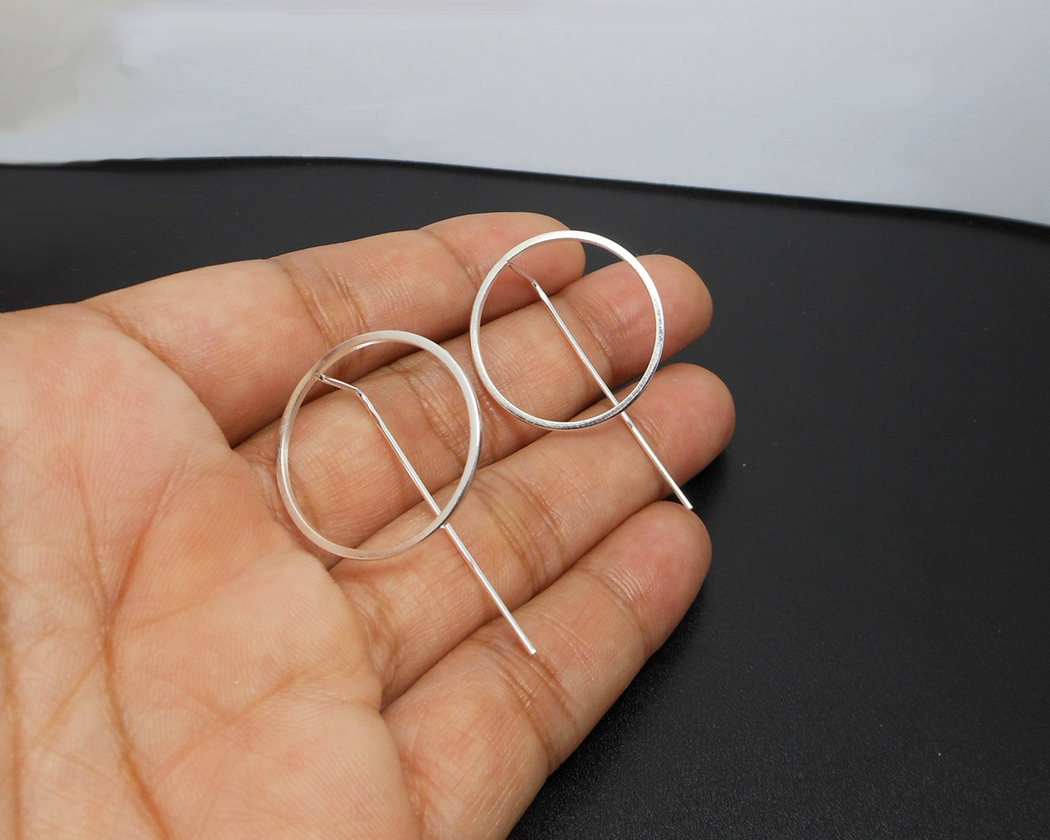 Pair of handmade circle threader earrings held in a hand.