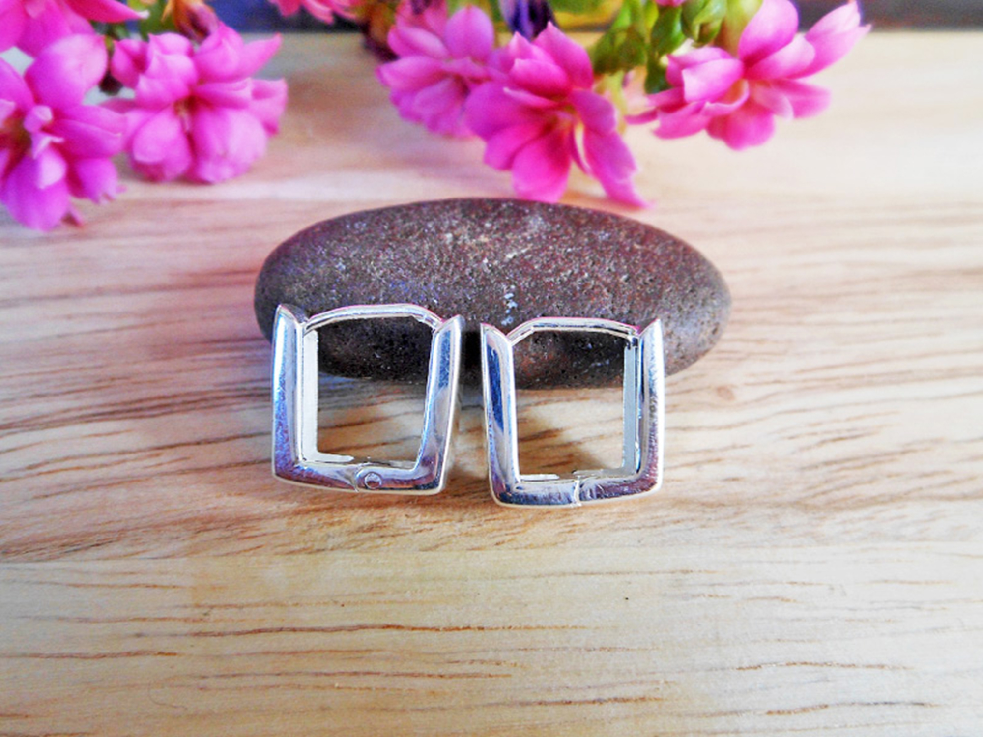 A pair of handmade 925 sterling silver flat square huggie earrings resting on a wooden surface.