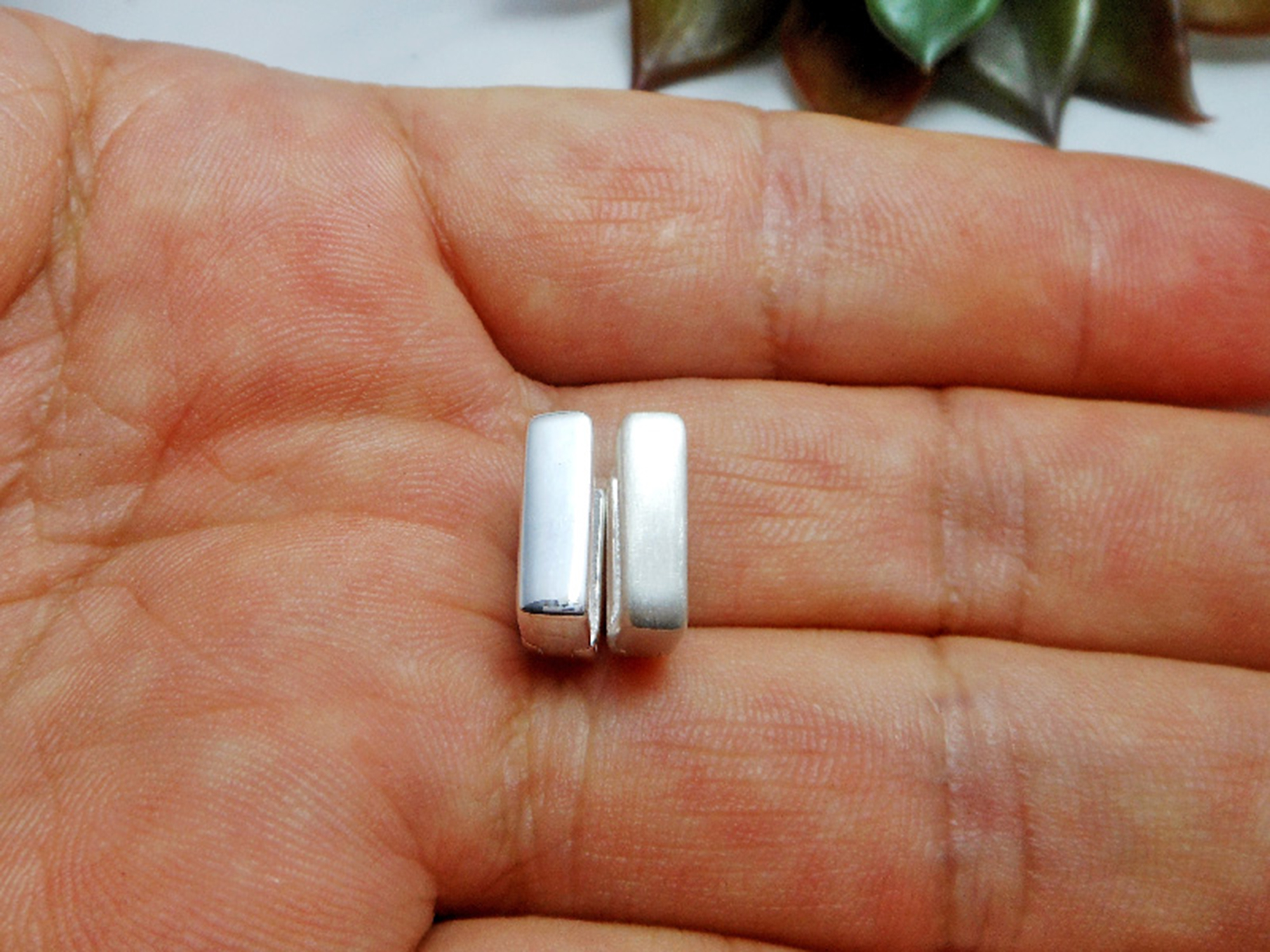 A close-up of a handmade 925 sterling silver flat square huggie earring held between fingers.