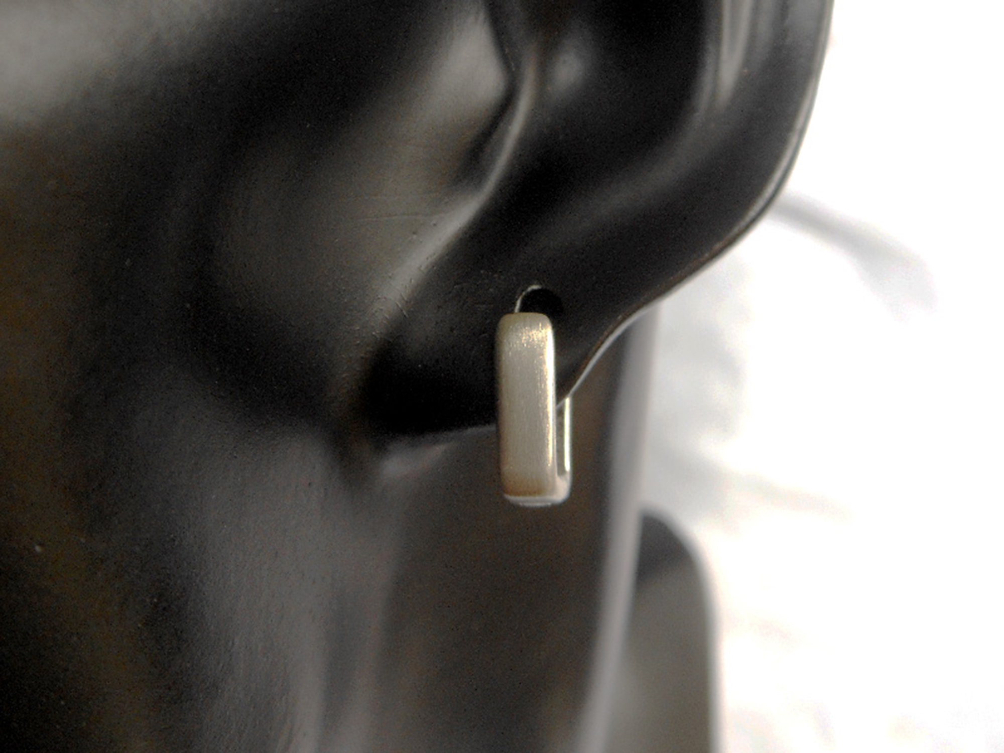 A close-up of a handmade 925 sterling silver flat square huggie earring on a dark mannequin ear.