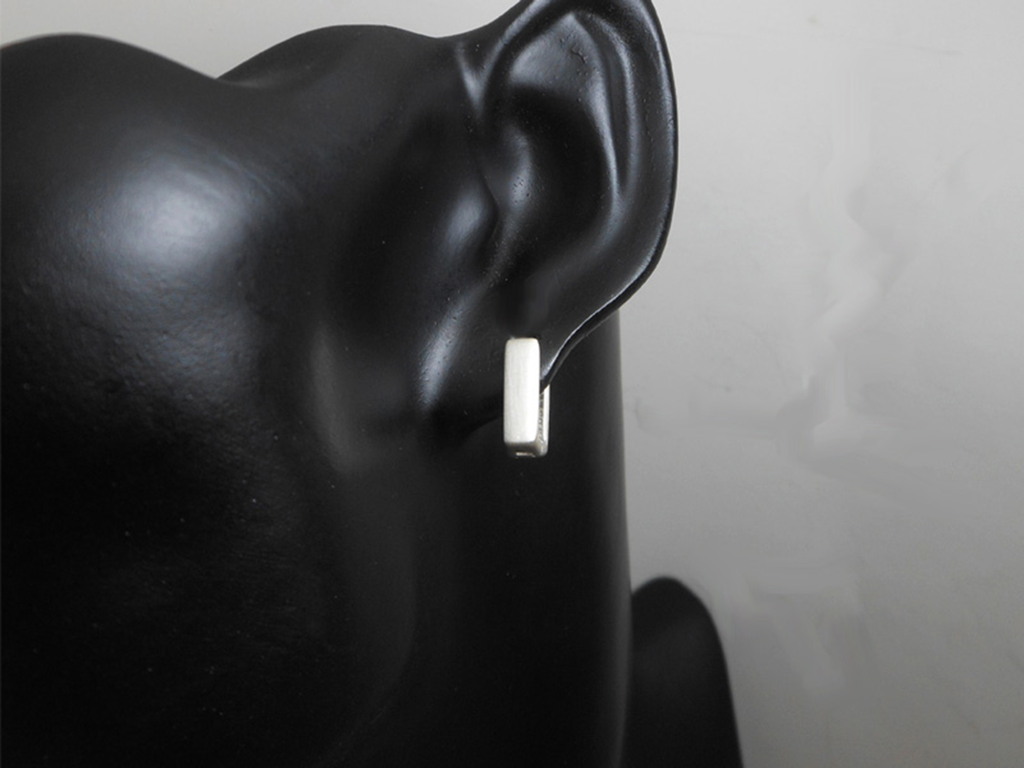 A close-up of a handmade 925 sterling silver flat square huggie earring on a dark mannequin ear.