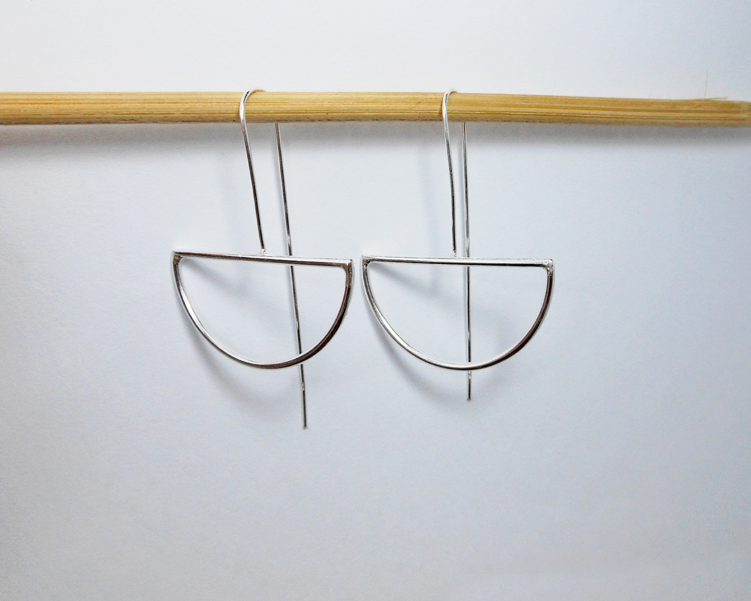 Silver half-moon threader earrings hanging from a wooden prop.
