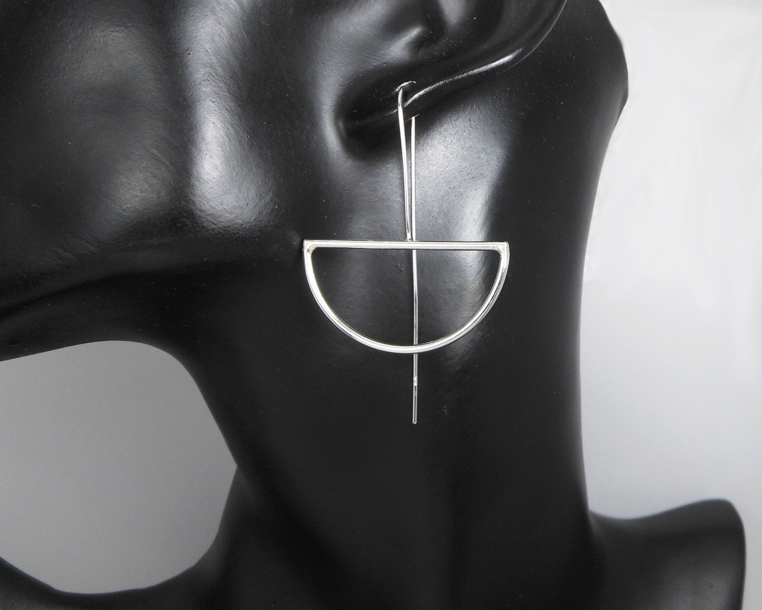Silver half-moon threader earrings displayed on a black mannequin bust.