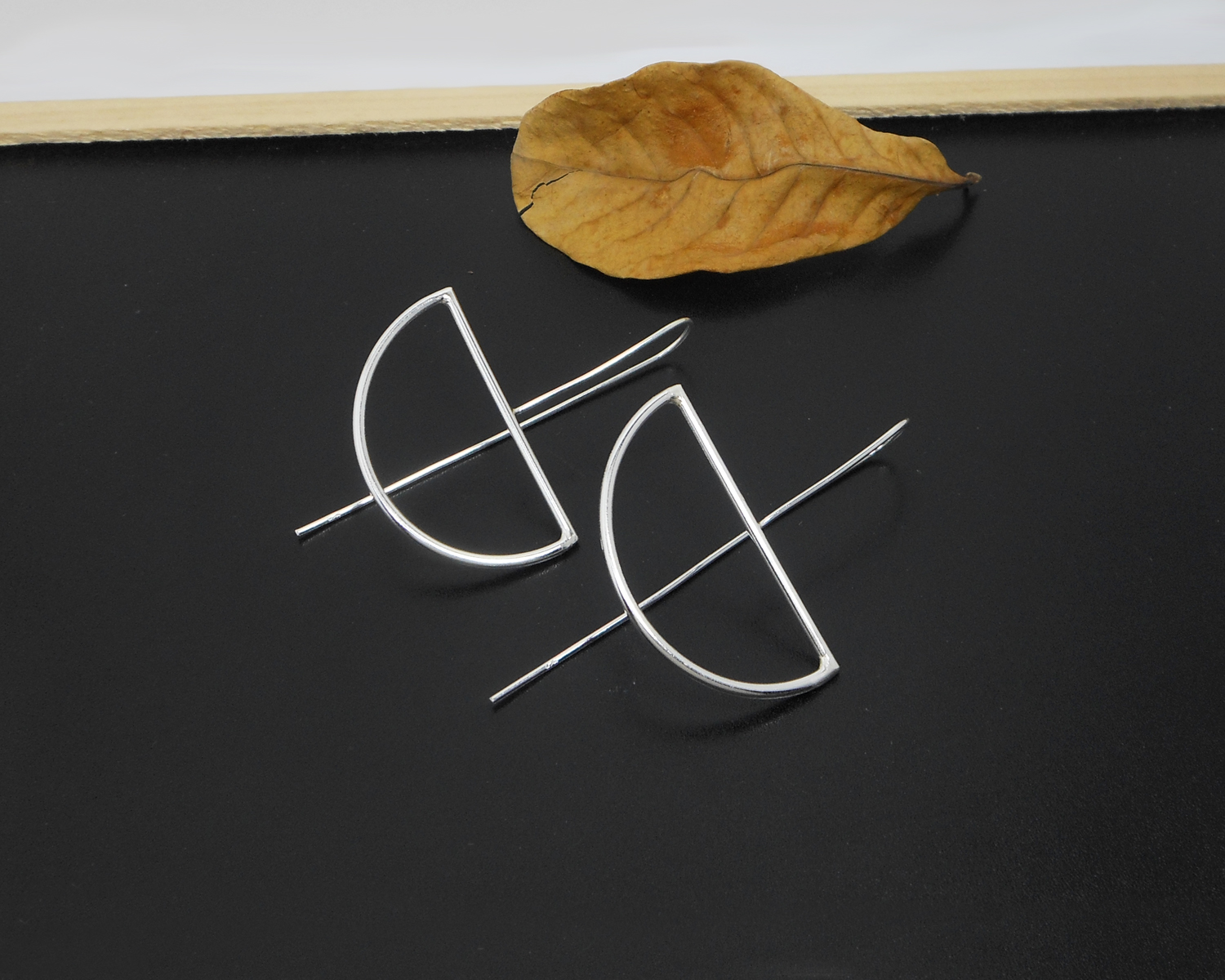 Pair of sterling silver half-moon threader earrings on a dark surface.