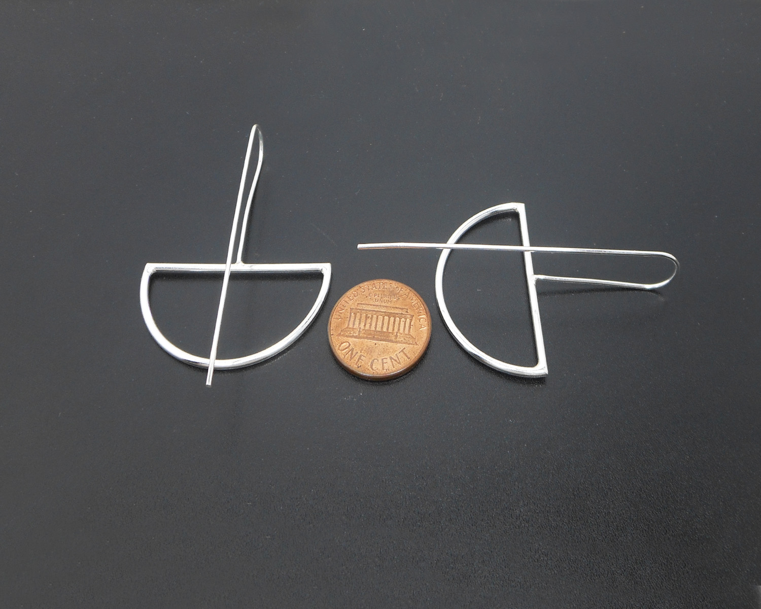 Silver half-moon threader earrings displayed next to a coin for size reference.