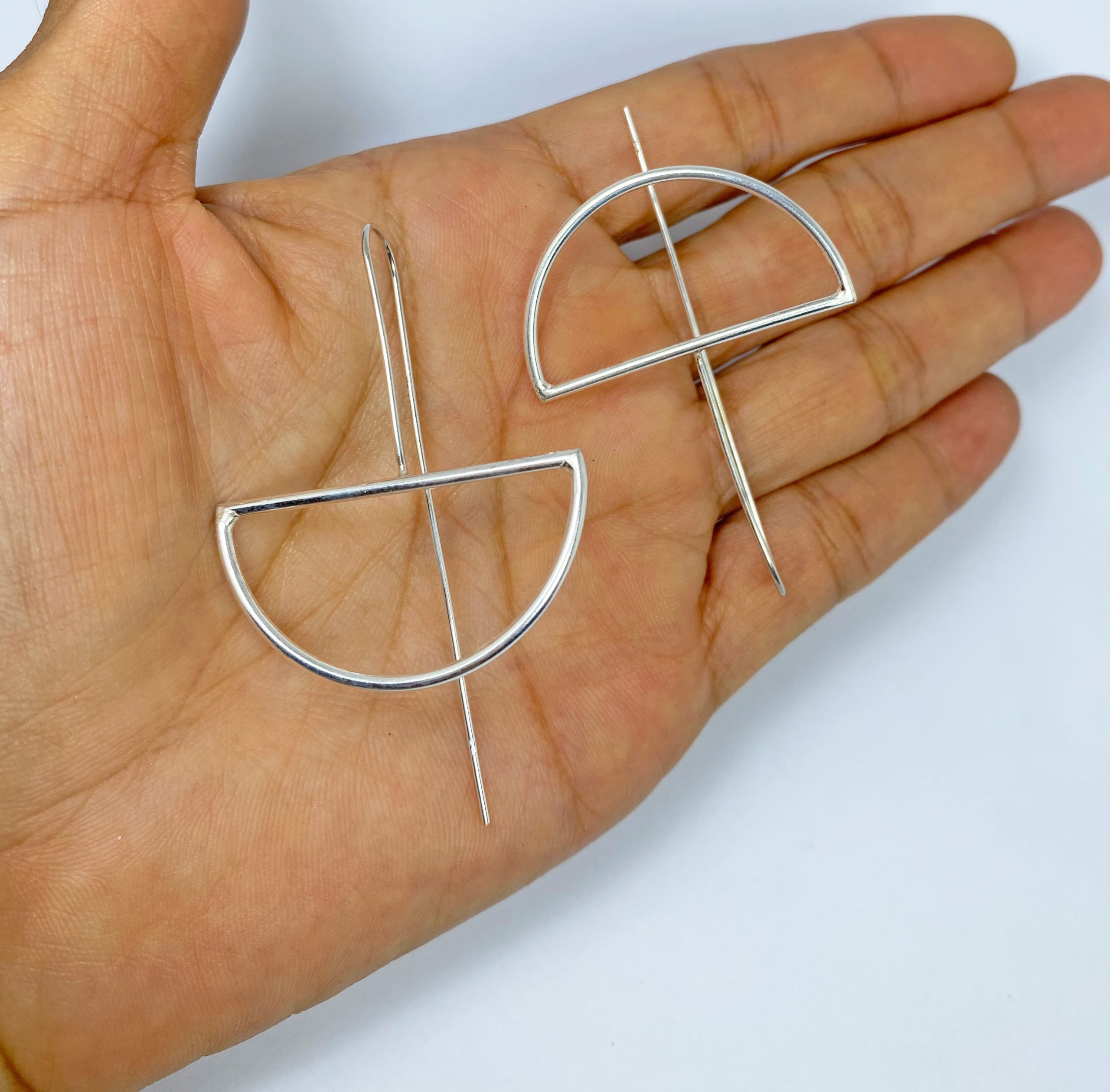 Pair of handmade silver half-moon threader earrings held in a hand.