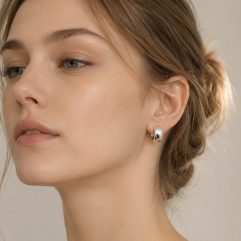 Close-up portrait of a woman wearing small, polished 925 sterling silver round dome huggie hoop earrings.