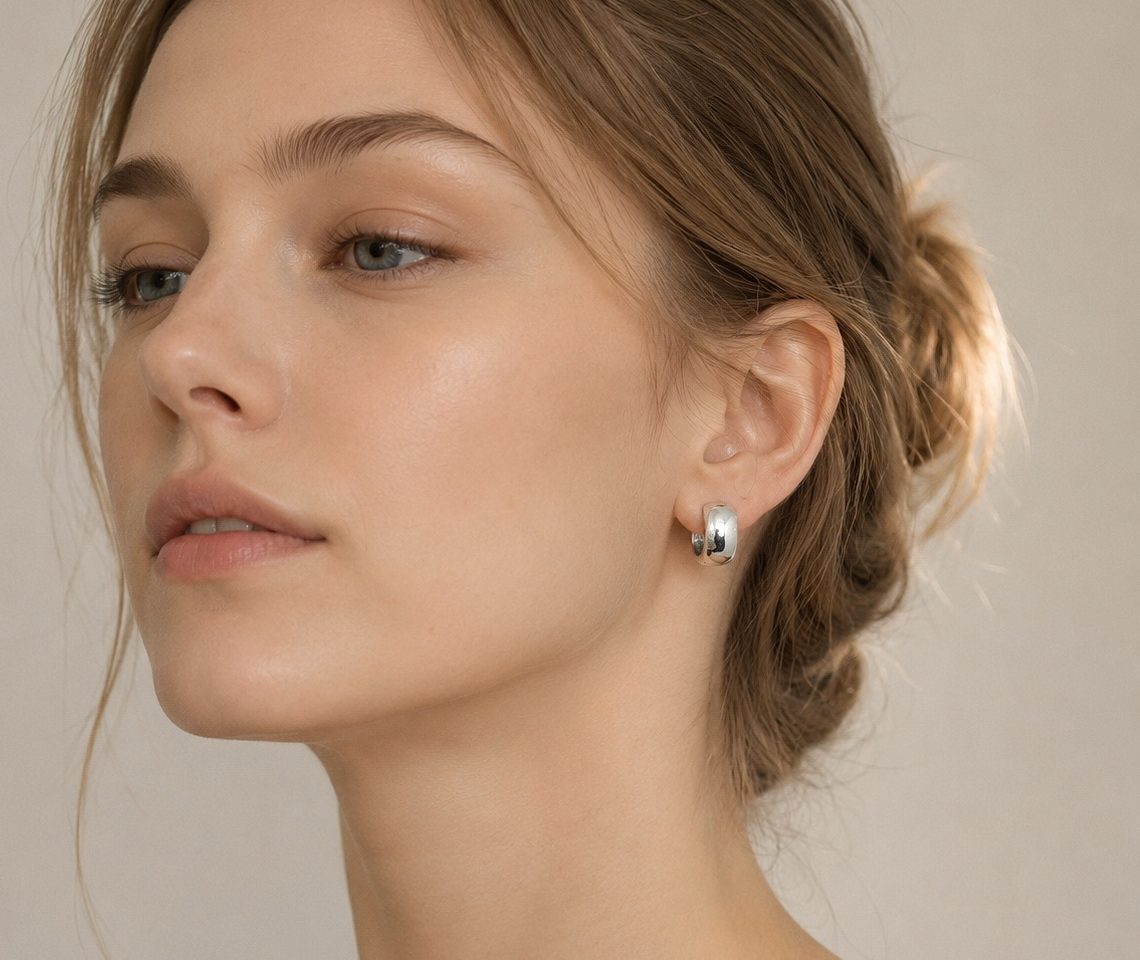 Close-up portrait of a woman wearing small, polished 925 sterling silver round dome huggie hoop earrings.