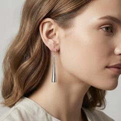 A close-up side profile of a woman wearing minimalist, long, polished sterling silver cone-shaped dangle earrings.