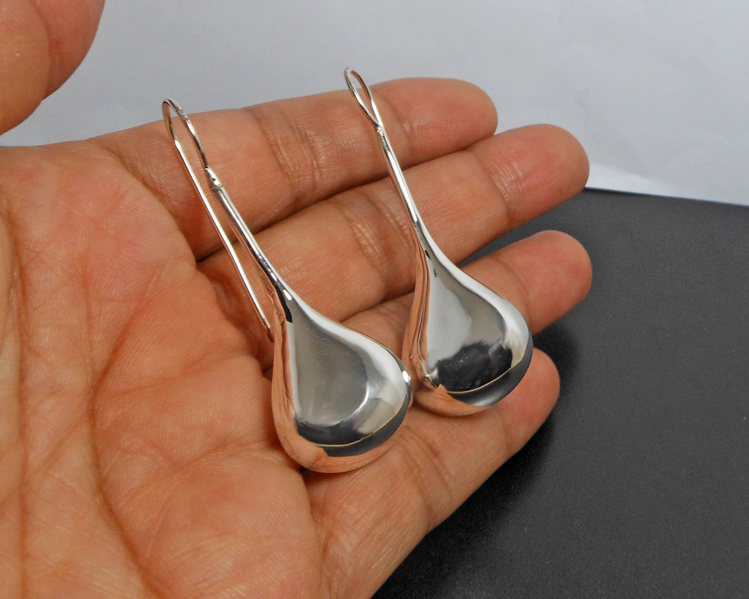 Handheld view of long teardrop threader earrings.