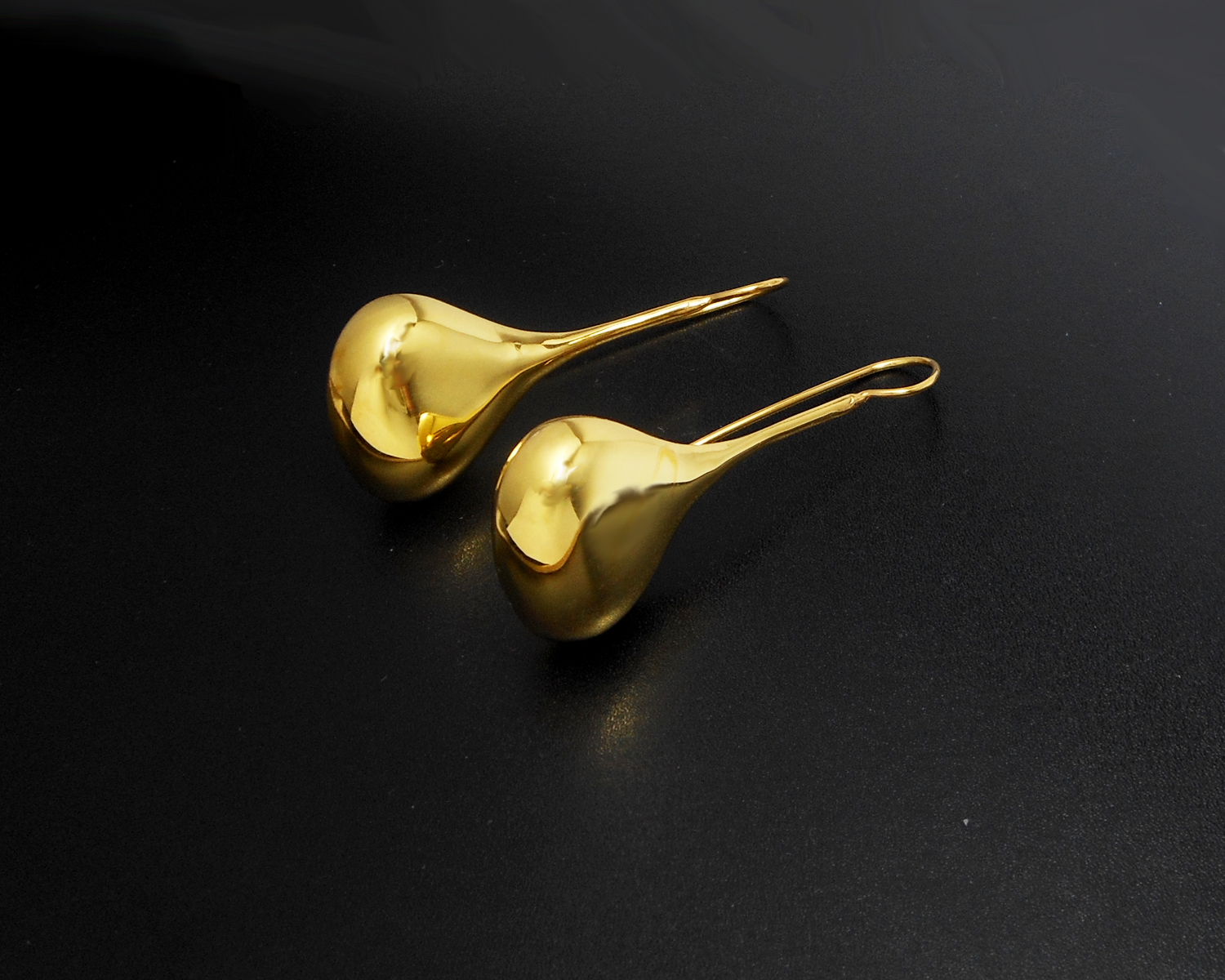 Close-up of long gold plated teardrop threader earrings on a dark background.