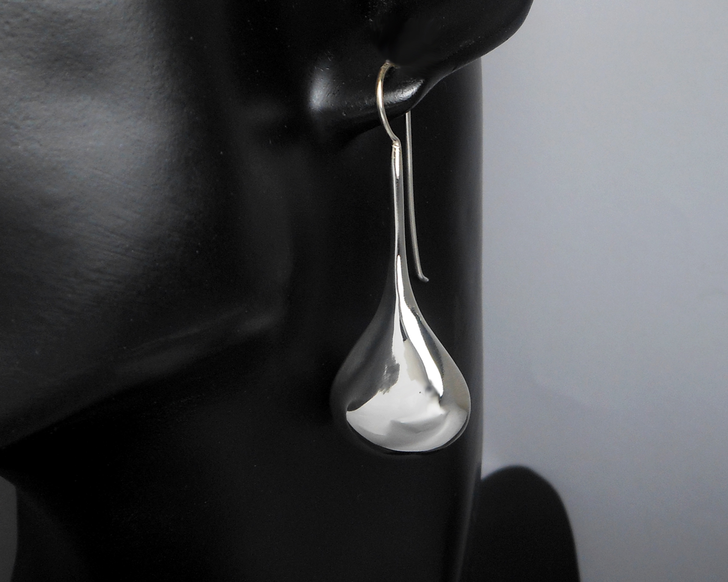 Long teardrop threader earrings displayed on a stand.