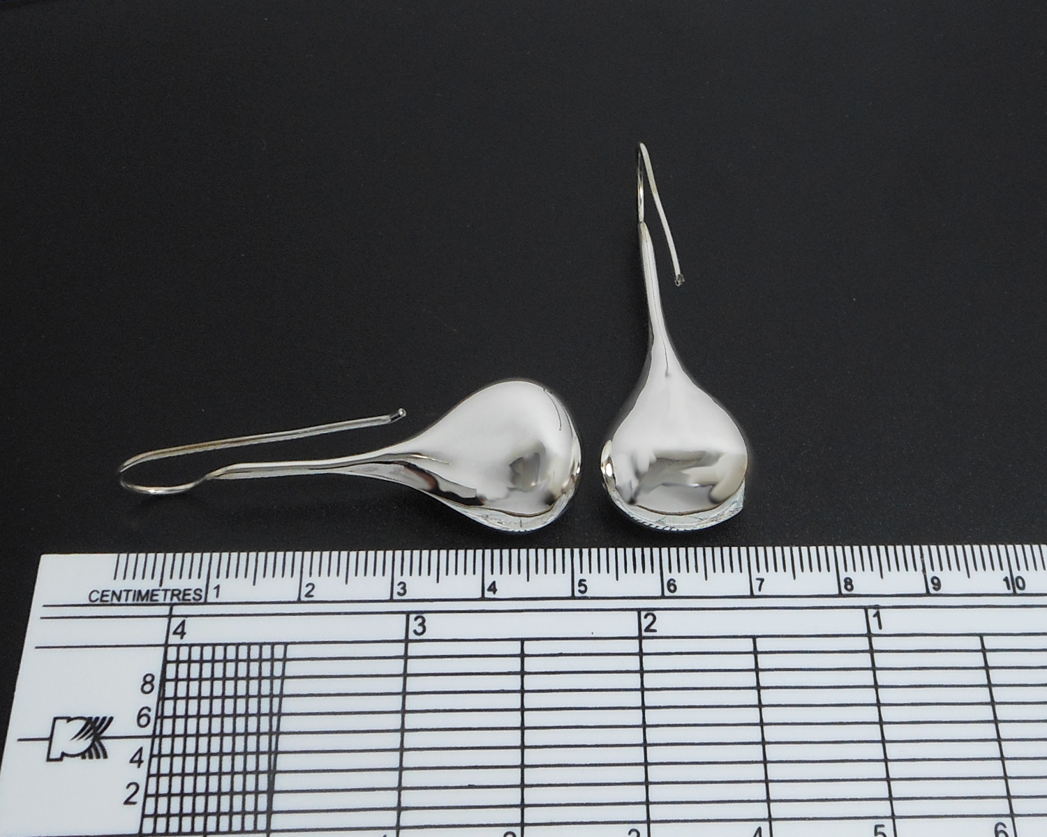 Long teardrop threader earrings displayed next to a measuring tool for size reference.