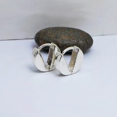 A pair of handcrafted 925 sterling silver V-button huggie hoop earrings resting next to a smooth dark stone.