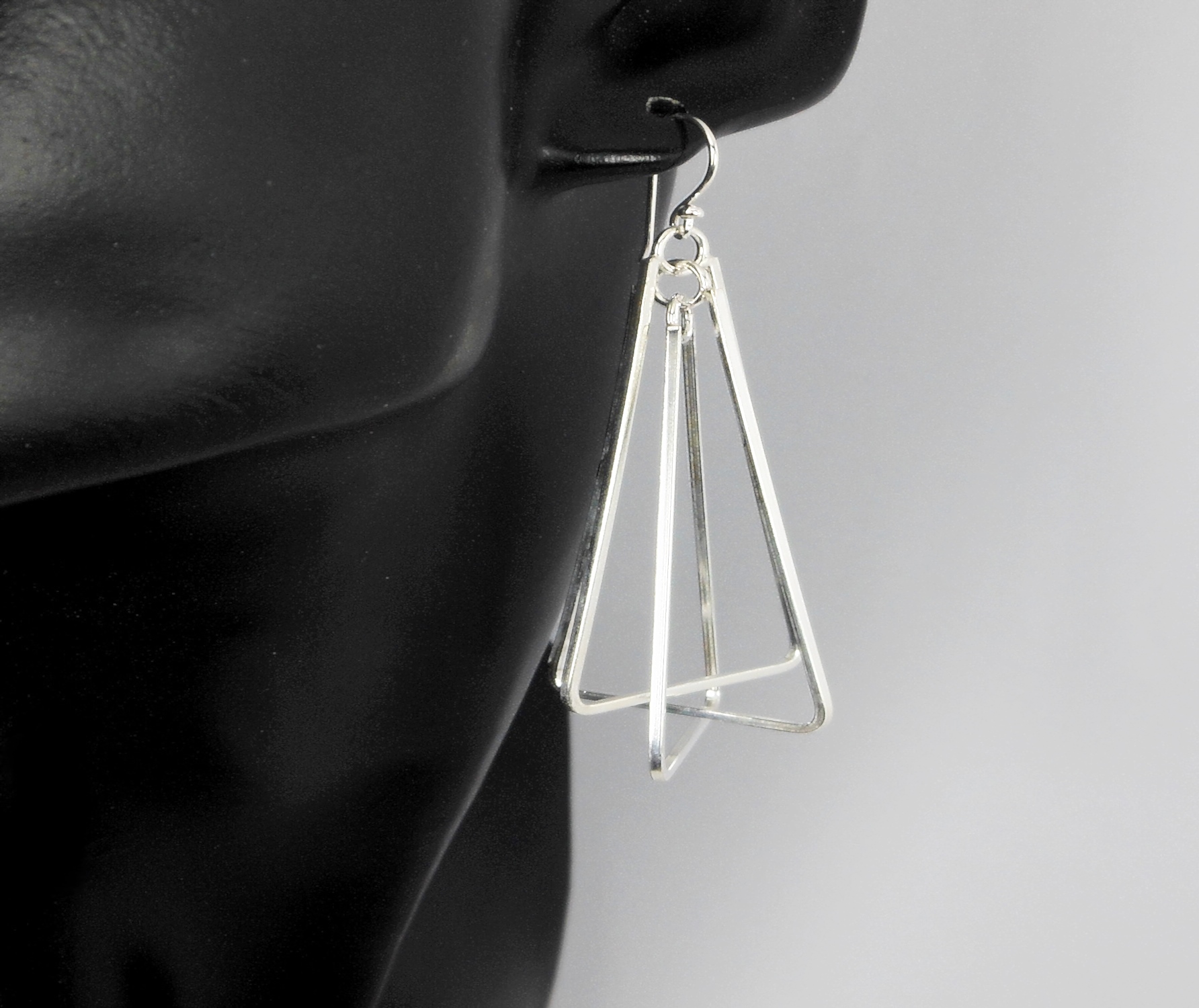A pair of handcrafted 925 sterling silver multi-spinning triangle pyramid drop earrings displayed on a black mannequin, highlighting their kinetic geometric design.