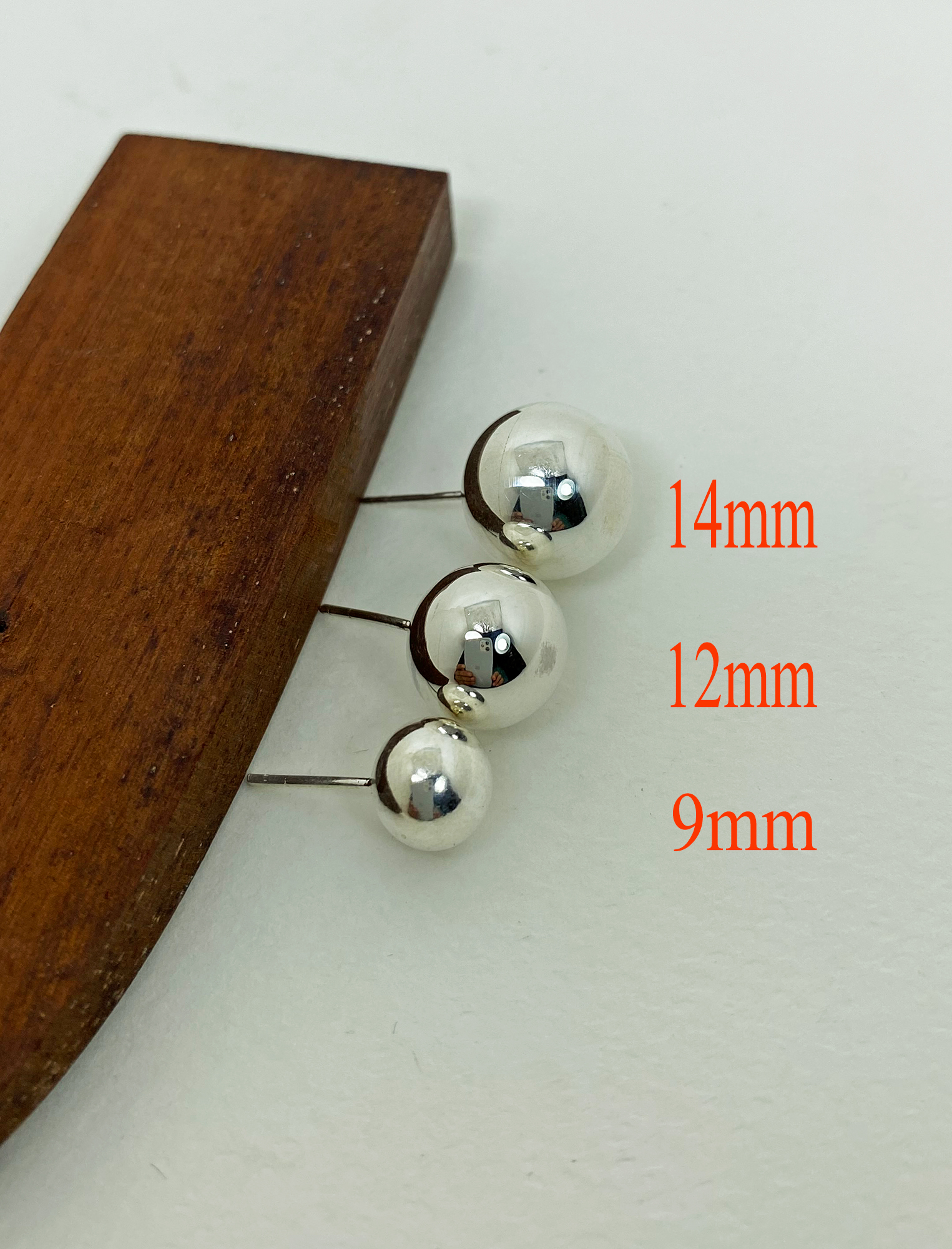 A collection of three handcrafted 925 sterling silver ball stud earrings in graduating sizes of 9mm, 12mm, and 14mm, displayed on a wooden surface.