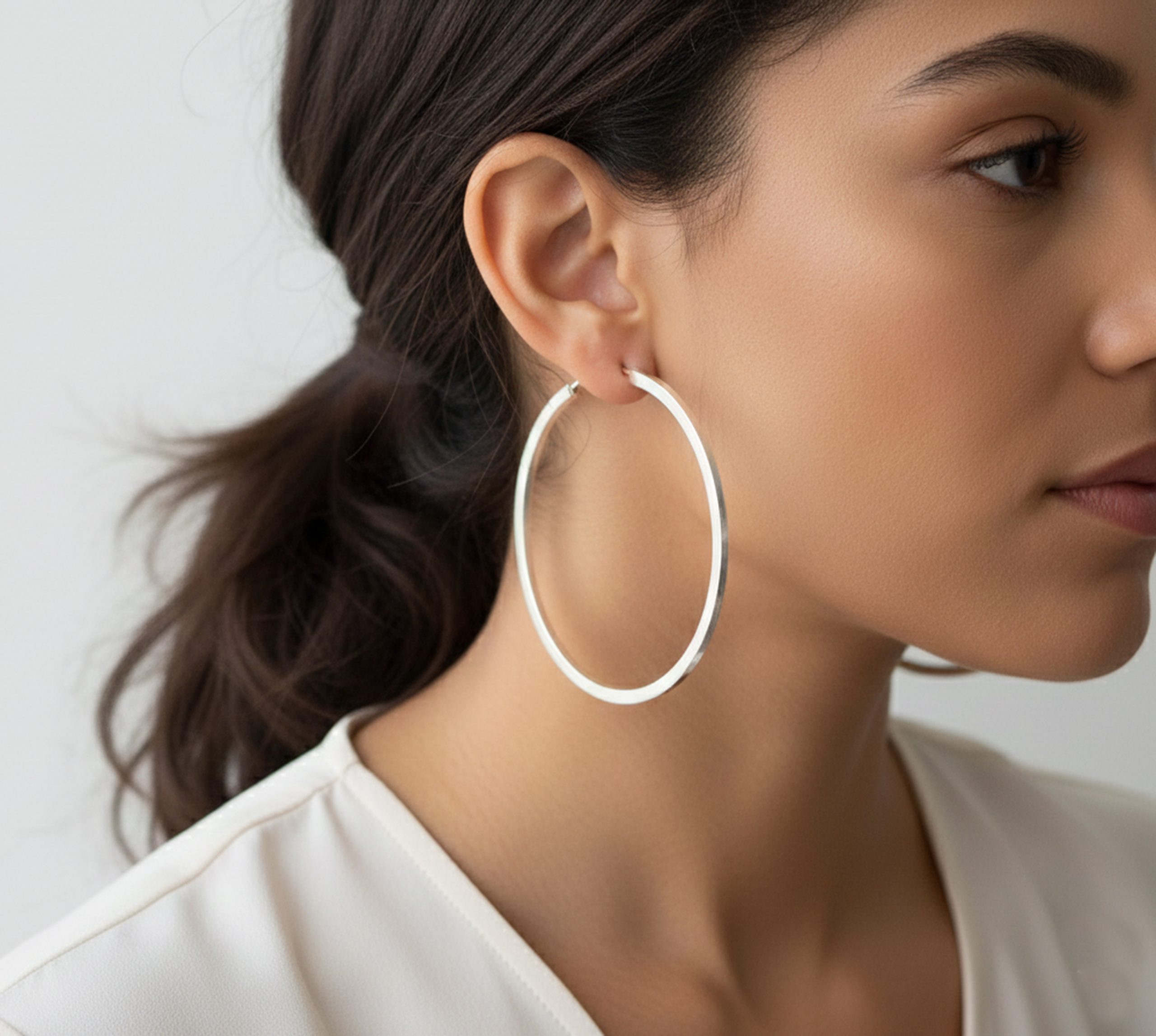 A close-up profile view of a woman wearing large 65mm handmade 925 sterling silver hoop earrings with a sleek square tube profile.