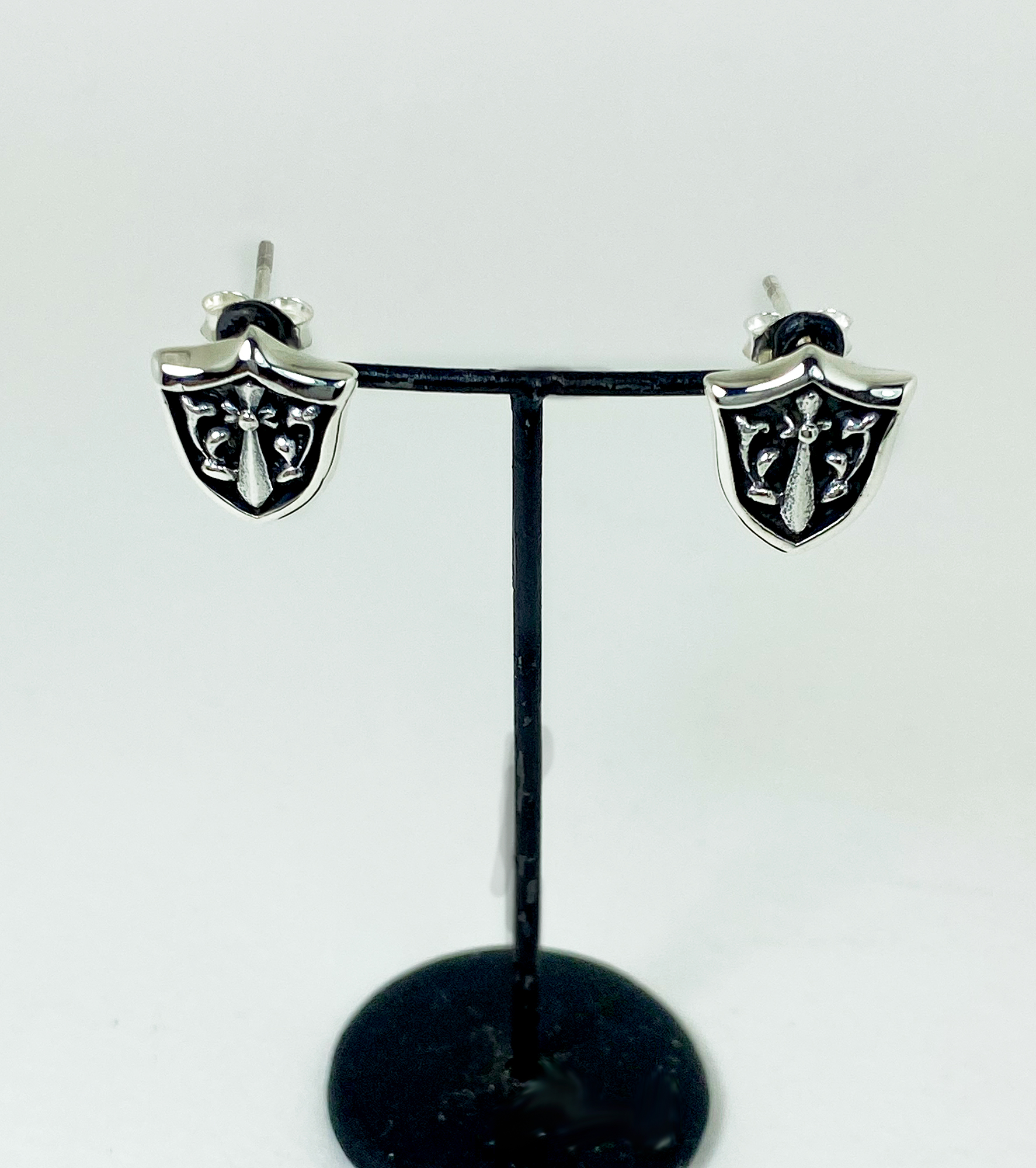 A pair of sterling silver sword and shield stud earrings displayed on a jewelry stand.
