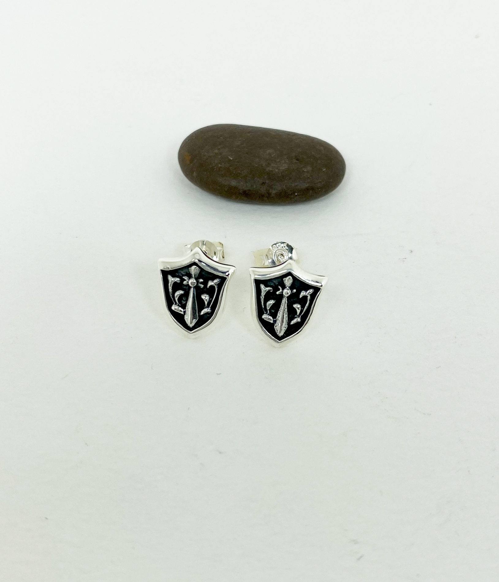Close-up of sterling silver sword and shield stud earrings on a white surface.