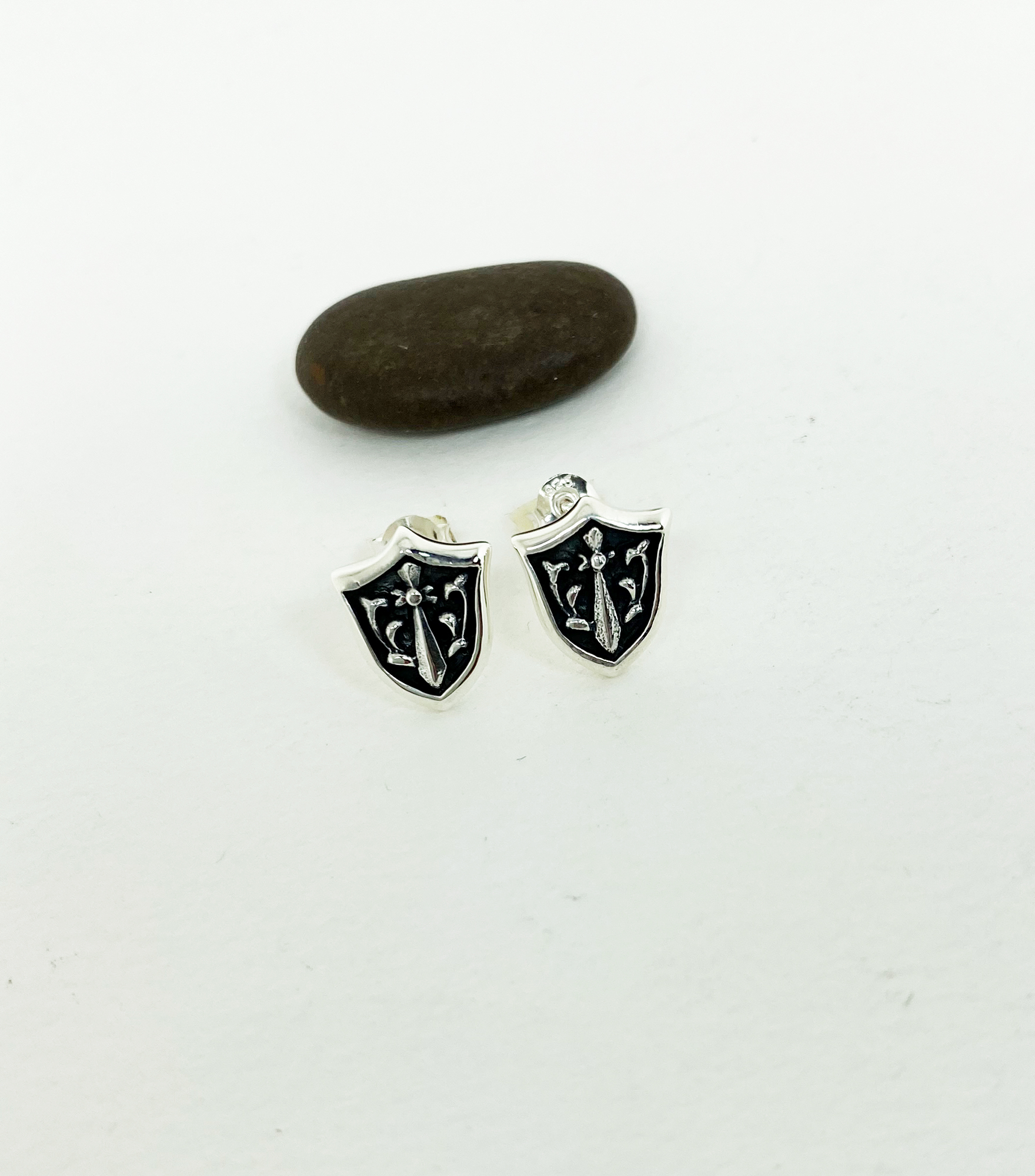 Sterling silver sword and shield stud earrings presented on a dark background.