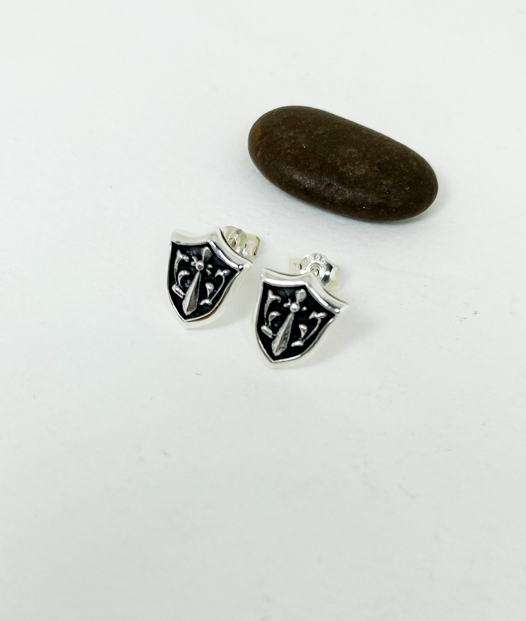 Pair of sterling silver sword and shield stud earrings shown from an angle.