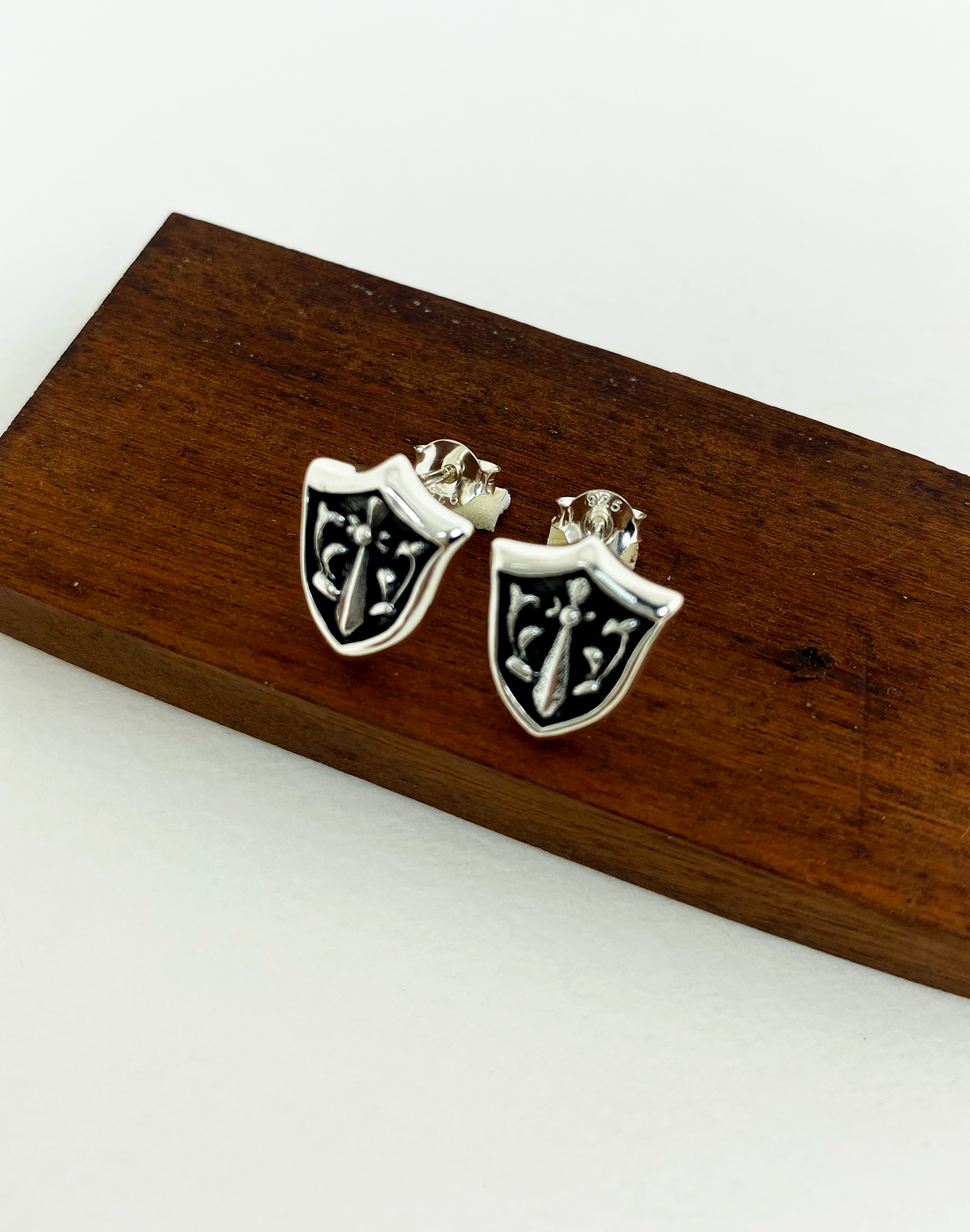 Sterling silver sword and shield stud earrings resting on a wooden surface.