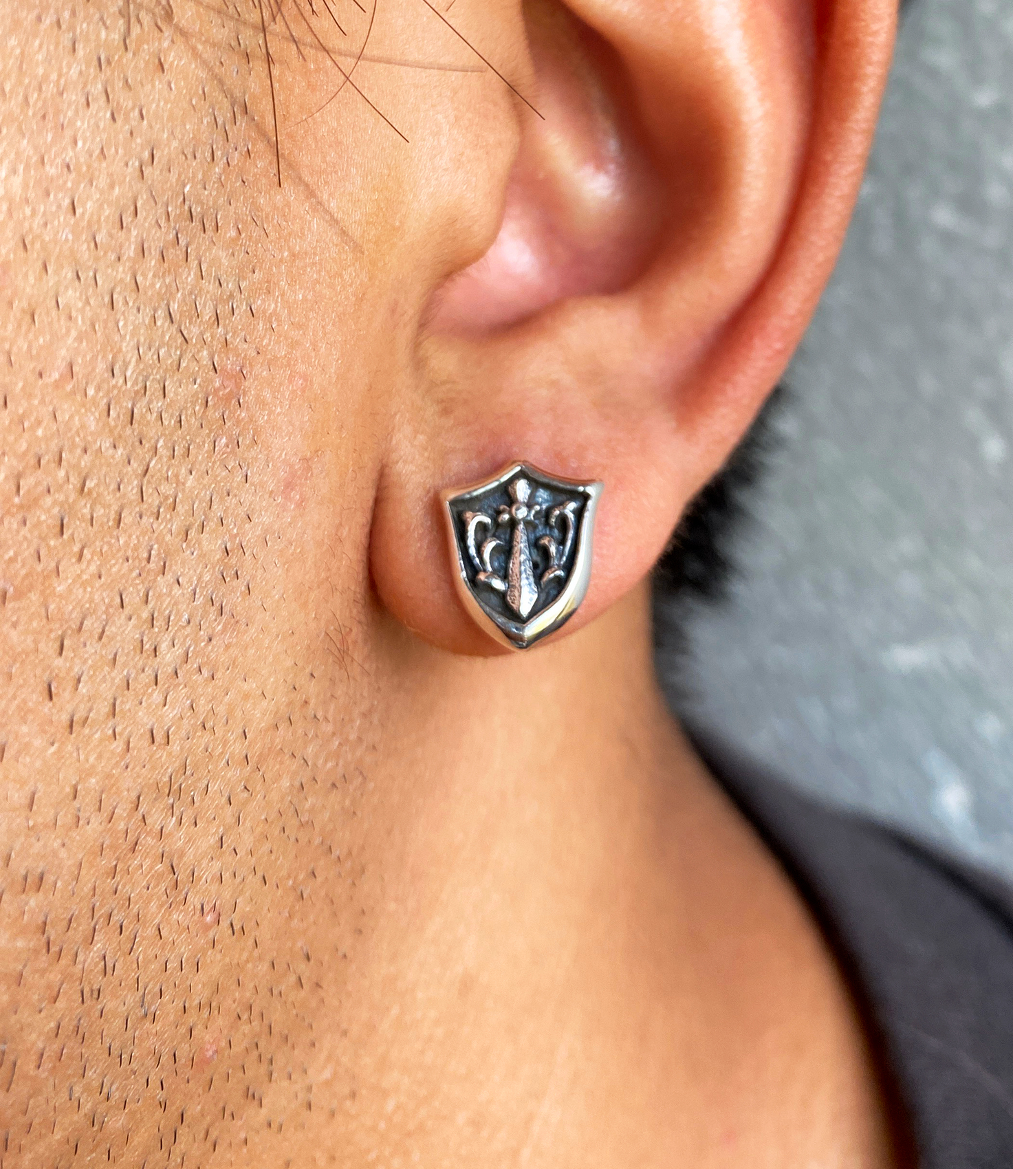 Close-up of a model wearing a sterling silver sword and shield stud earring.