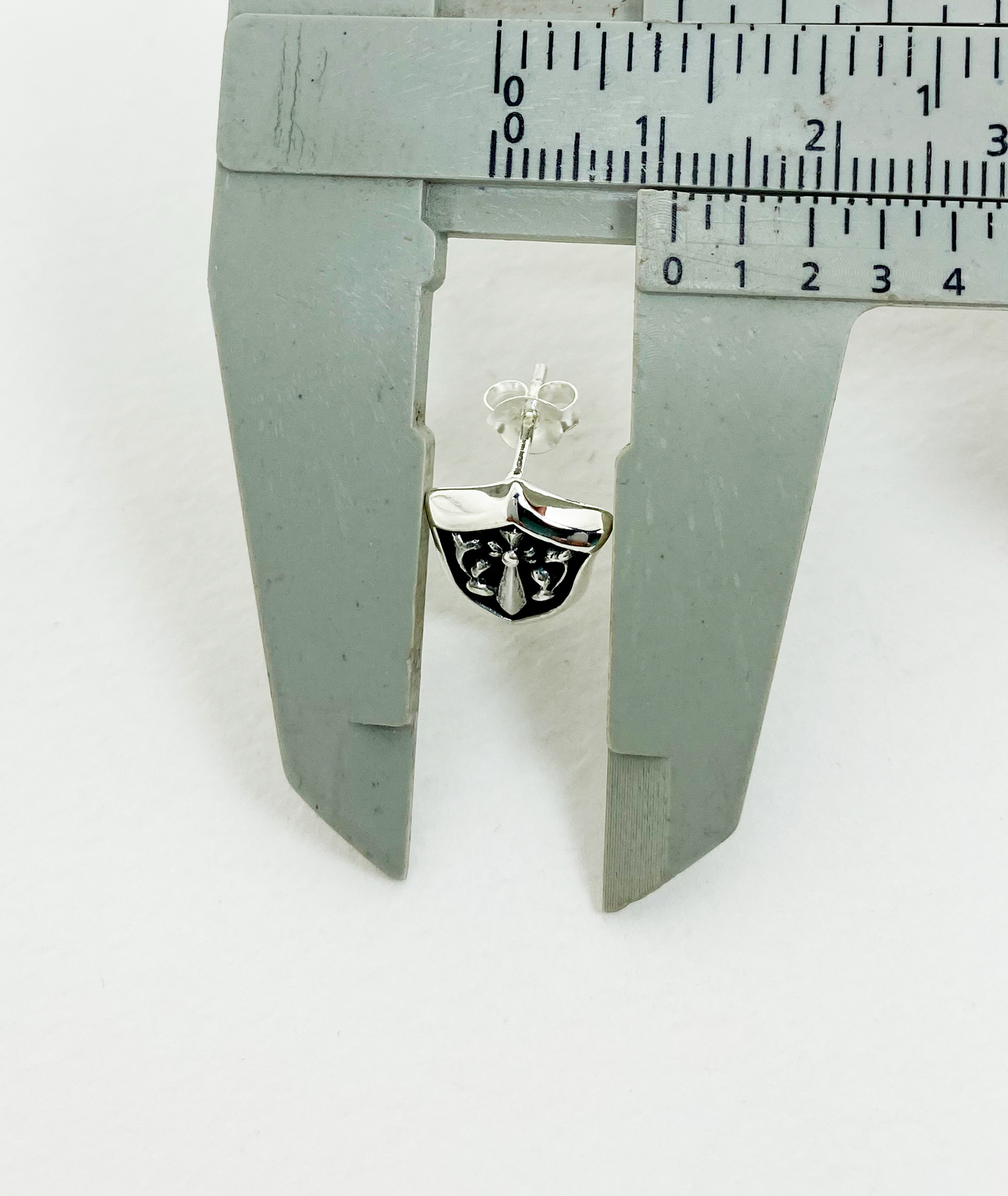 Sterling silver sword and shield stud earring being measured with calipers.
