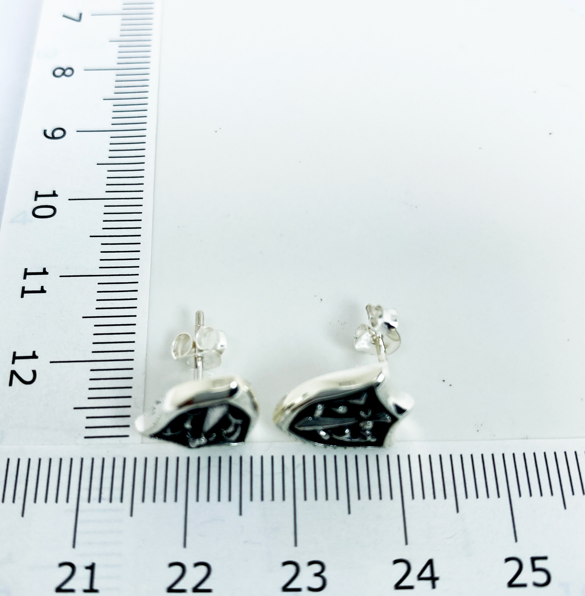 Sterling silver sword and shield stud earring shown next to a measuring tape for size reference.