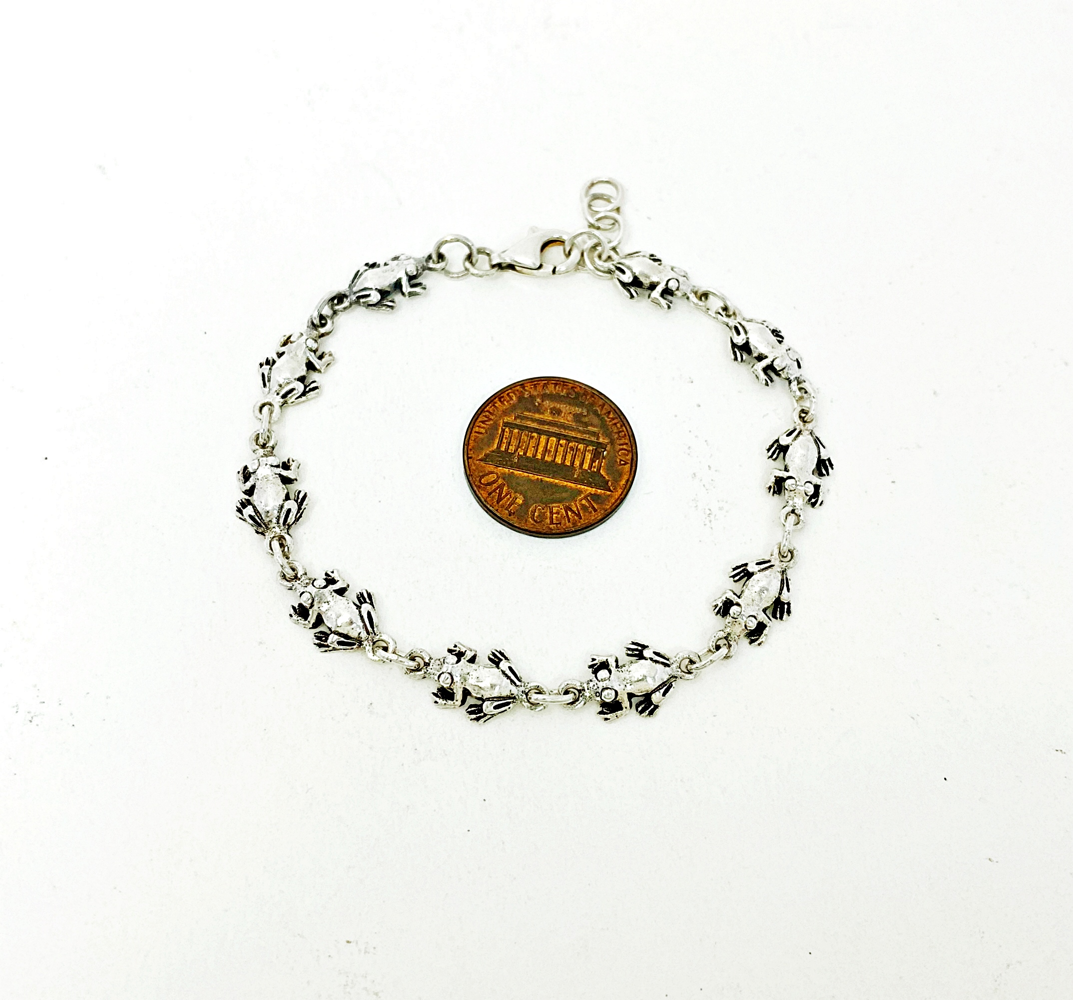 Flat lay of solid sterling silver frog link chain bracelet alongside a US penny for size reference.