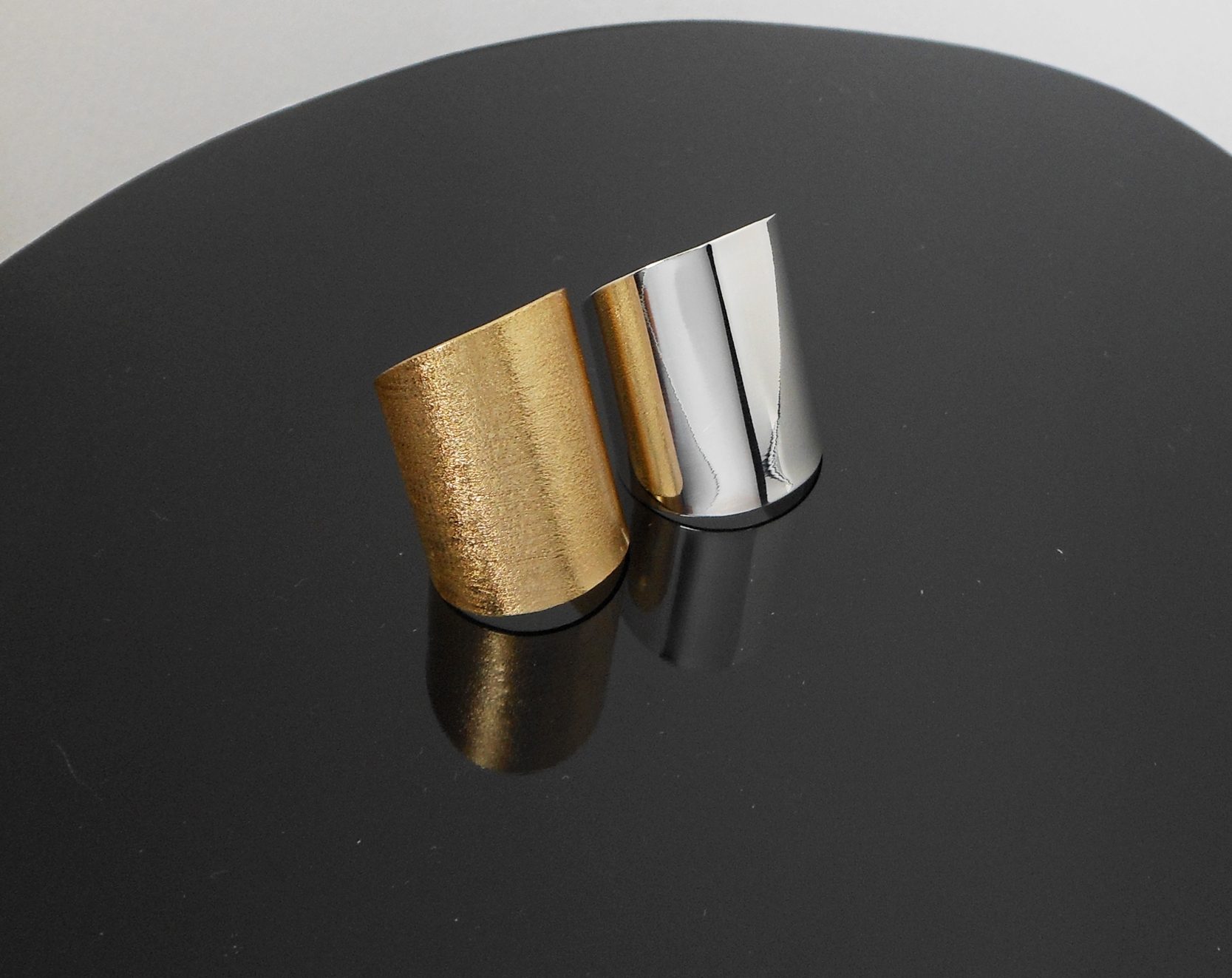 A handcrafted, wide flat band cuff ring made of 925 sterling silver, shown in both polished silver and matte gold-plated finishes against a rustic wood background.
