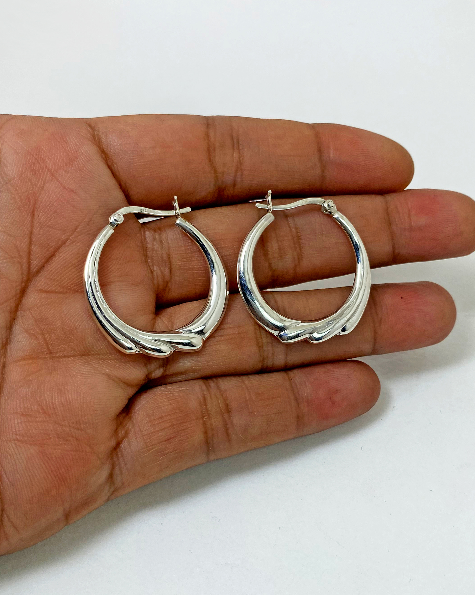 A pair of handcrafted 925 sterling silver hoop earrings featuring a unique puffy, textured flower-inspired design, displayed in a hand