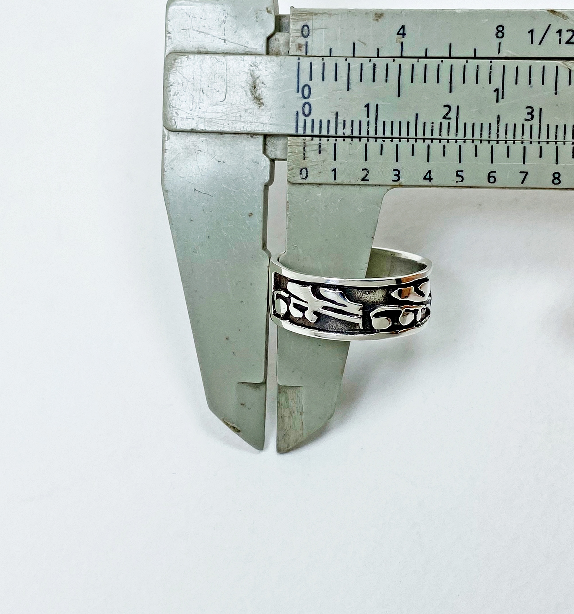 A close-up shot of a vernier caliper measuring the thickness of a 925 sterling silver leaf ring.