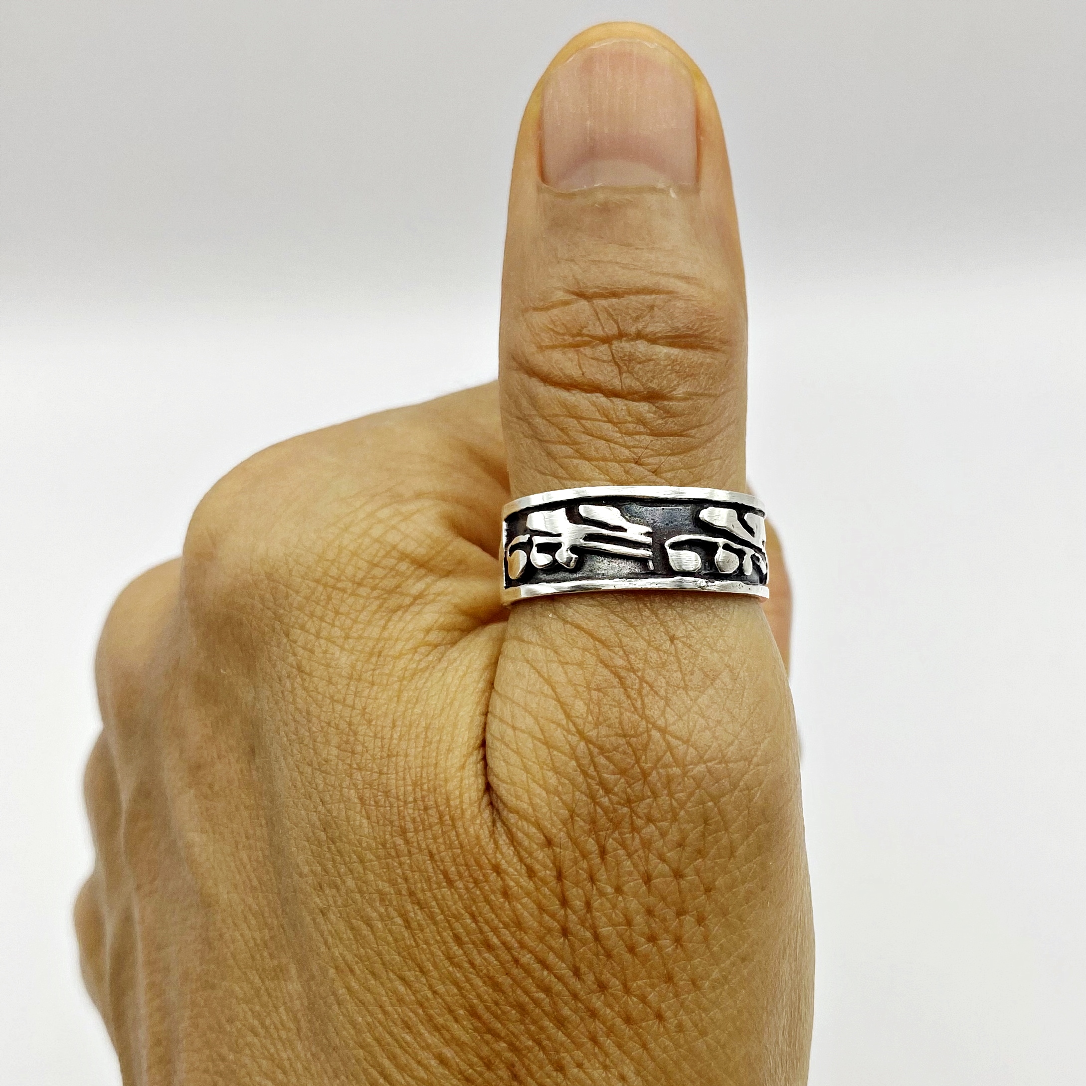 Close-up of a textured sterling silver leaf band ring worn on a person's thumb.
