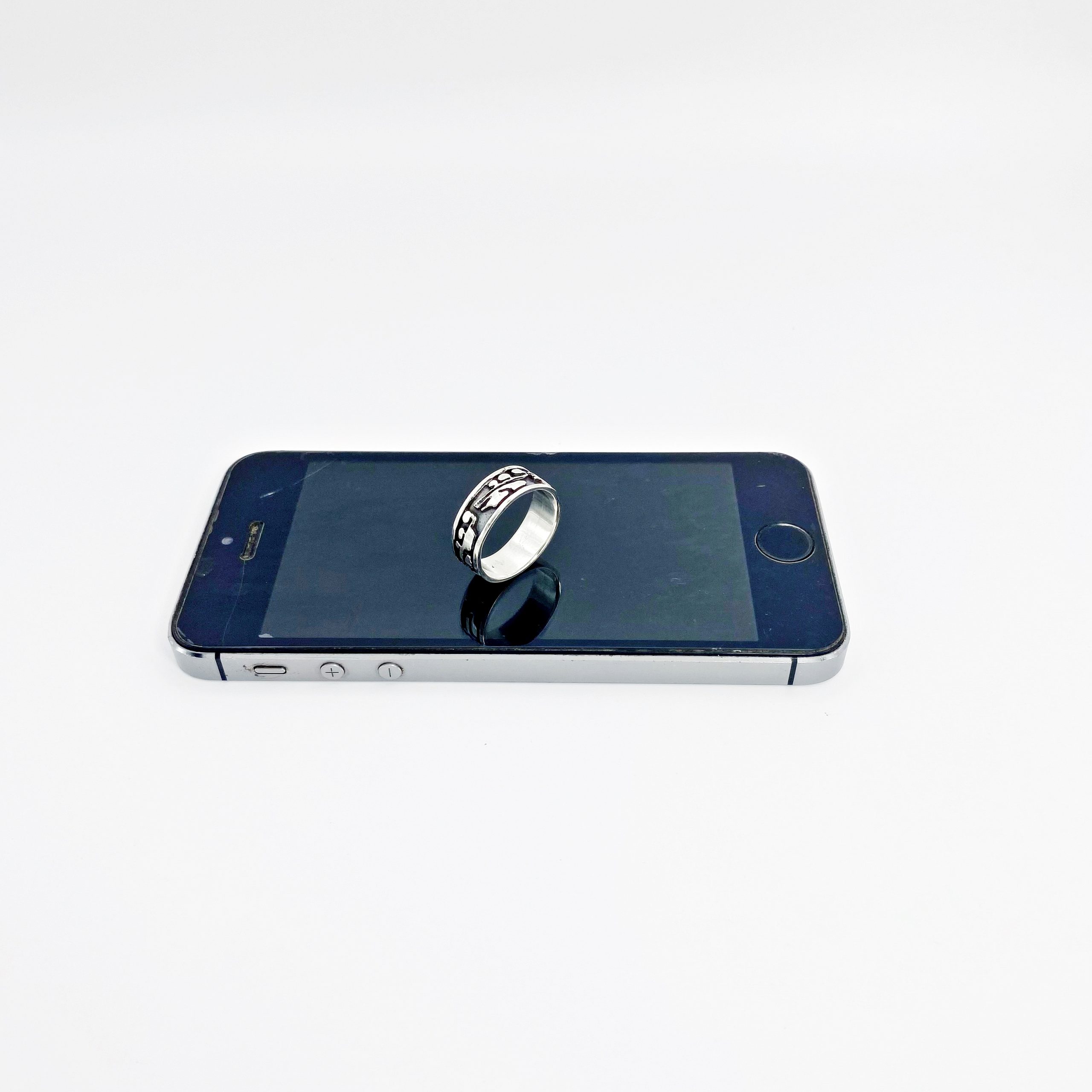 A silver band ring placed flat on top of a dark smartphone screen. File 8 (Ring right side view)