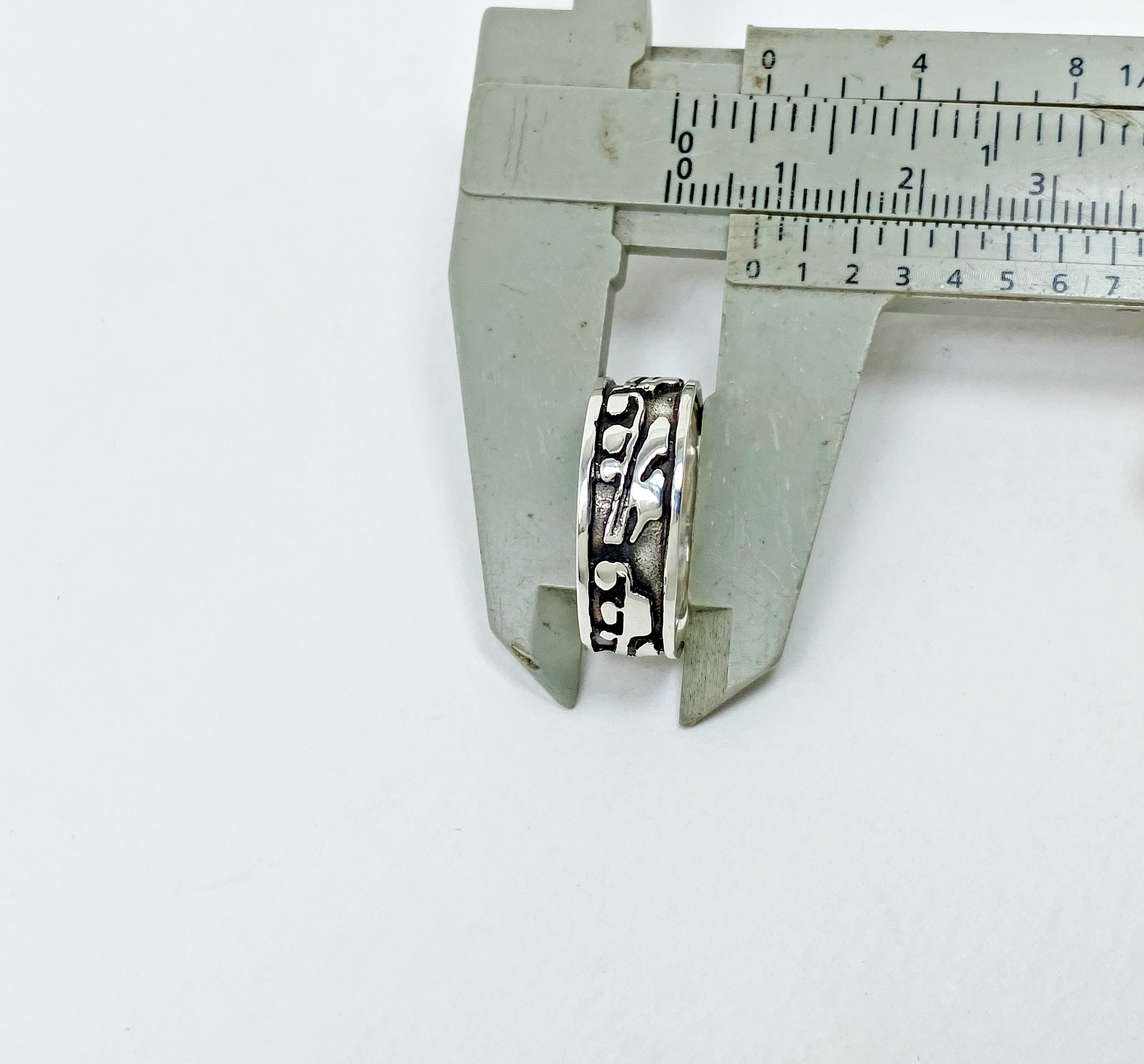 Close-up of a silver ring's band width being measured precisely with a caliper tool.
