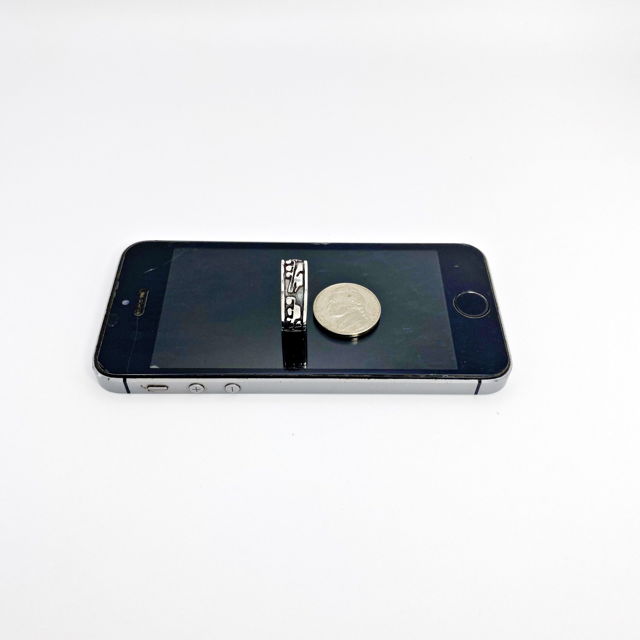 The silver band ring laid flat next to a coin on a black surface for scale comparison.