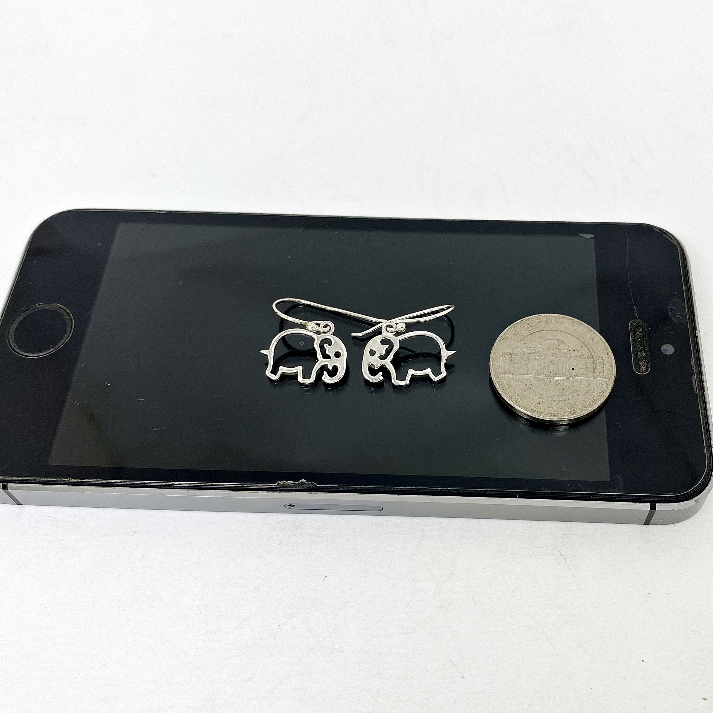 Cutout Elephant Dangle Earrings placed on top of a black smartphone for size reference.