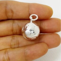 Small handmade silver soccer ball pendant held between fingers to show the physical scale.
