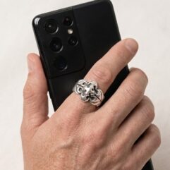 Close-up of a hand wearing the silver quatrefoil shield ring while holding a black smartphone.