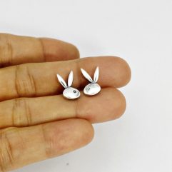 A extreme close-up shot of a person holding a pair of small, silver rabbit head stud earrings on their fingertips.