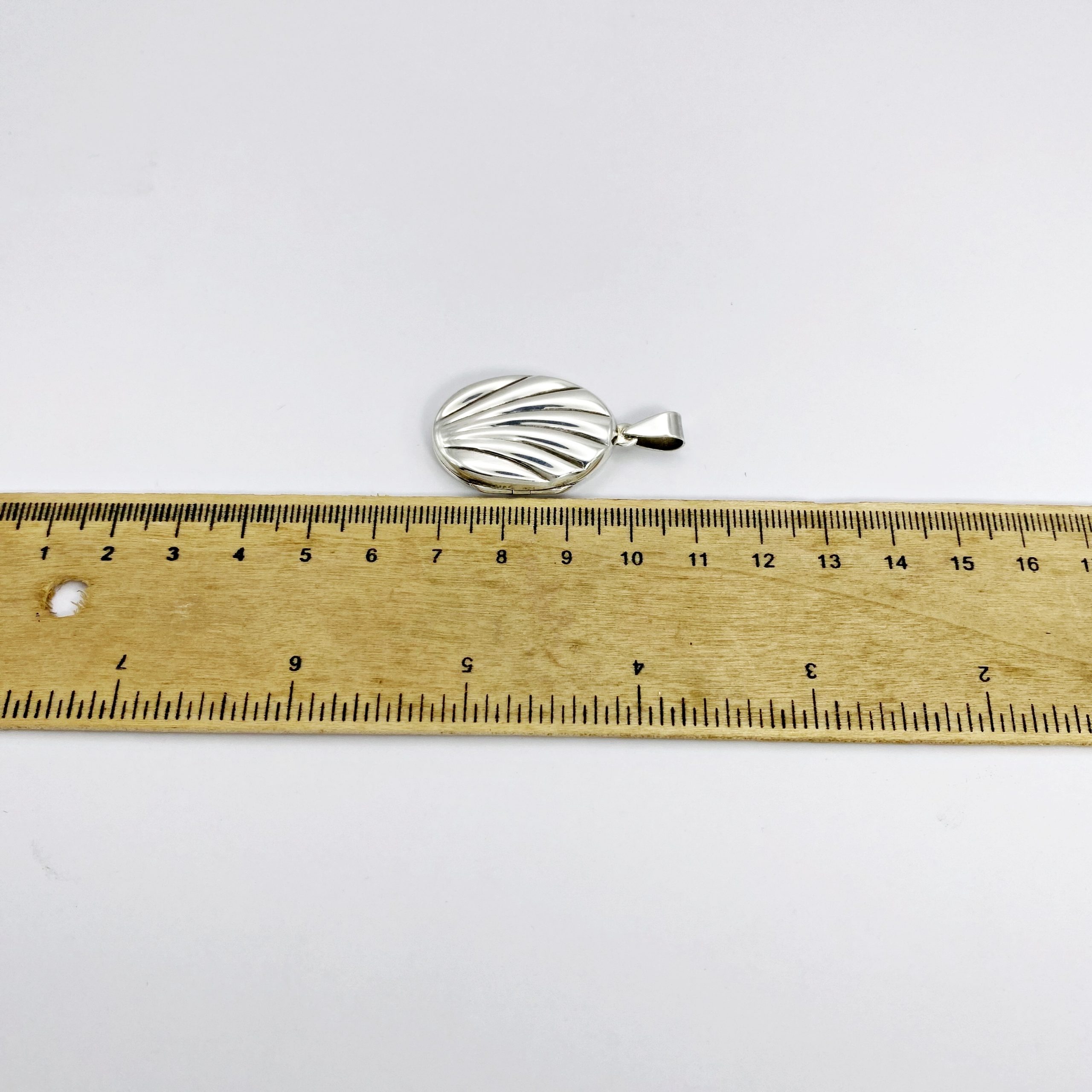 A 925 silver oval locket pendant measured against a yellow ruler to show its full height including the bail.