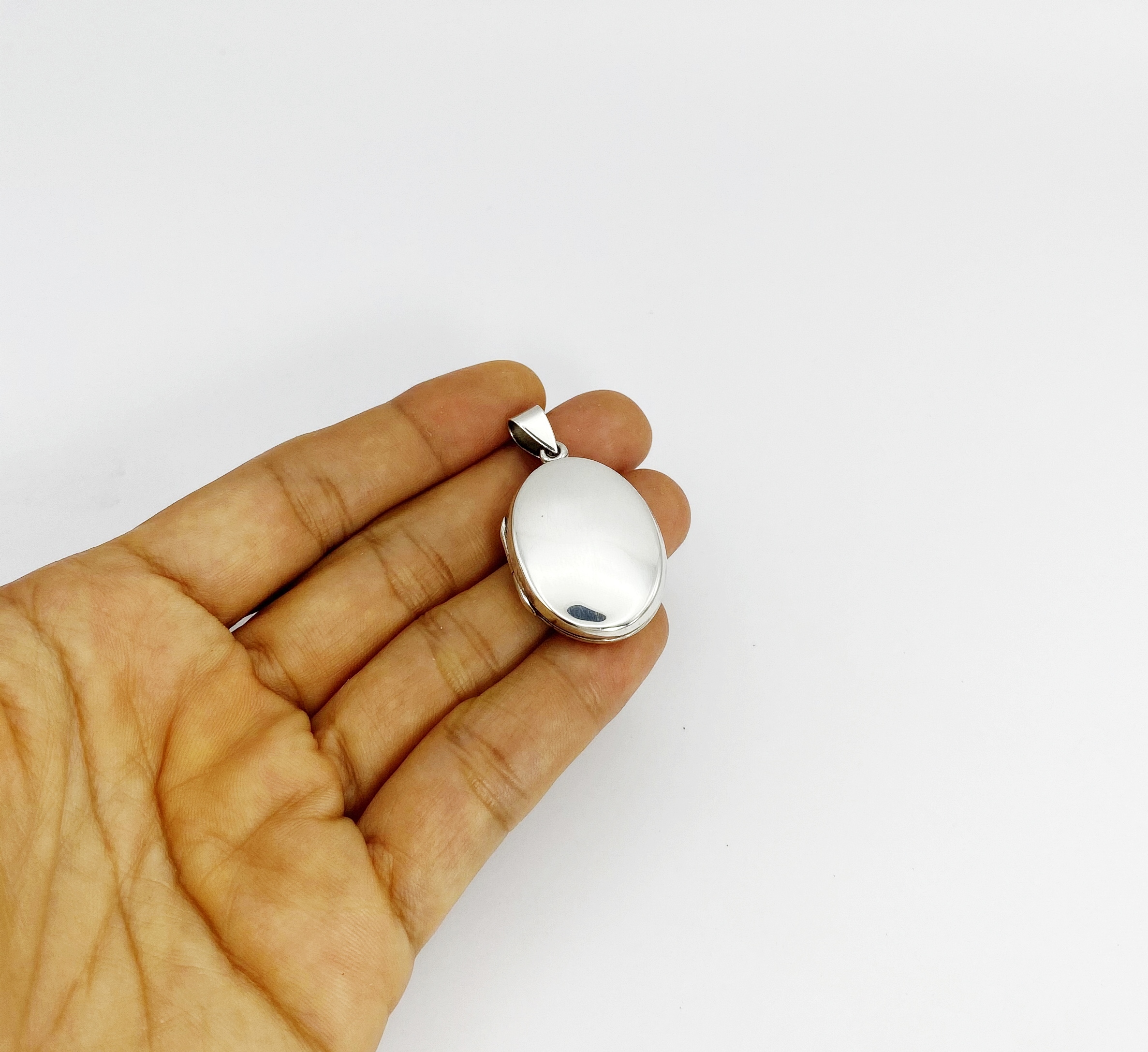 Hand holding the smooth high-polish reverse side of an oval 925 sterling silver keepsake locket pendant.