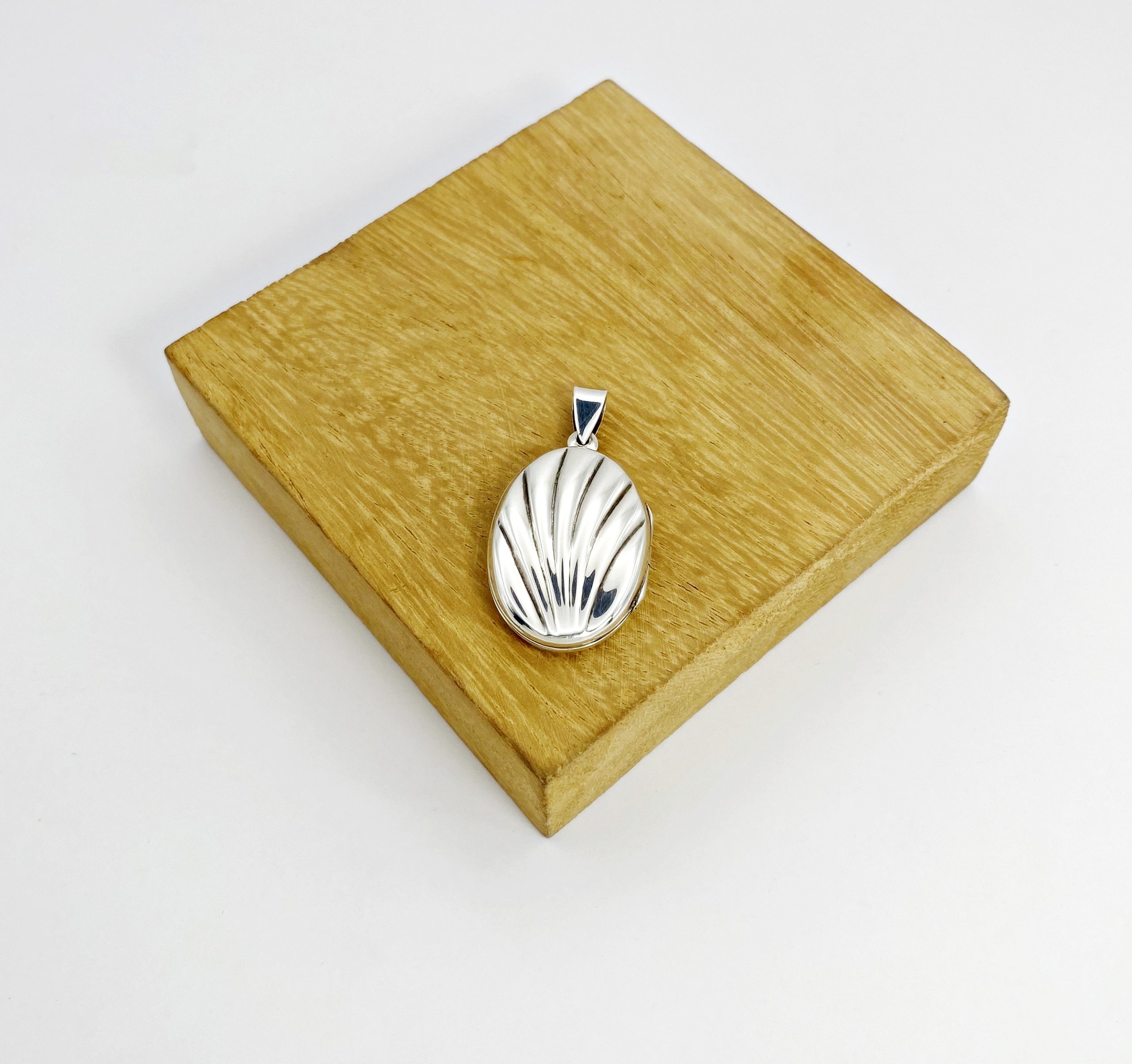 Front view of an oxidized silver keepsake locket pendant resting flat on a square wood block display.